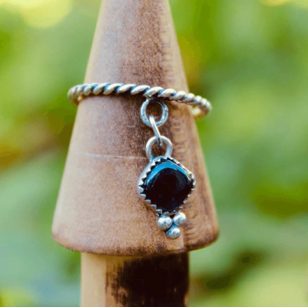 A piece of jewelry with a black gemstone pendant hanging from a twisted silver chain, displayed on a wooden cone.