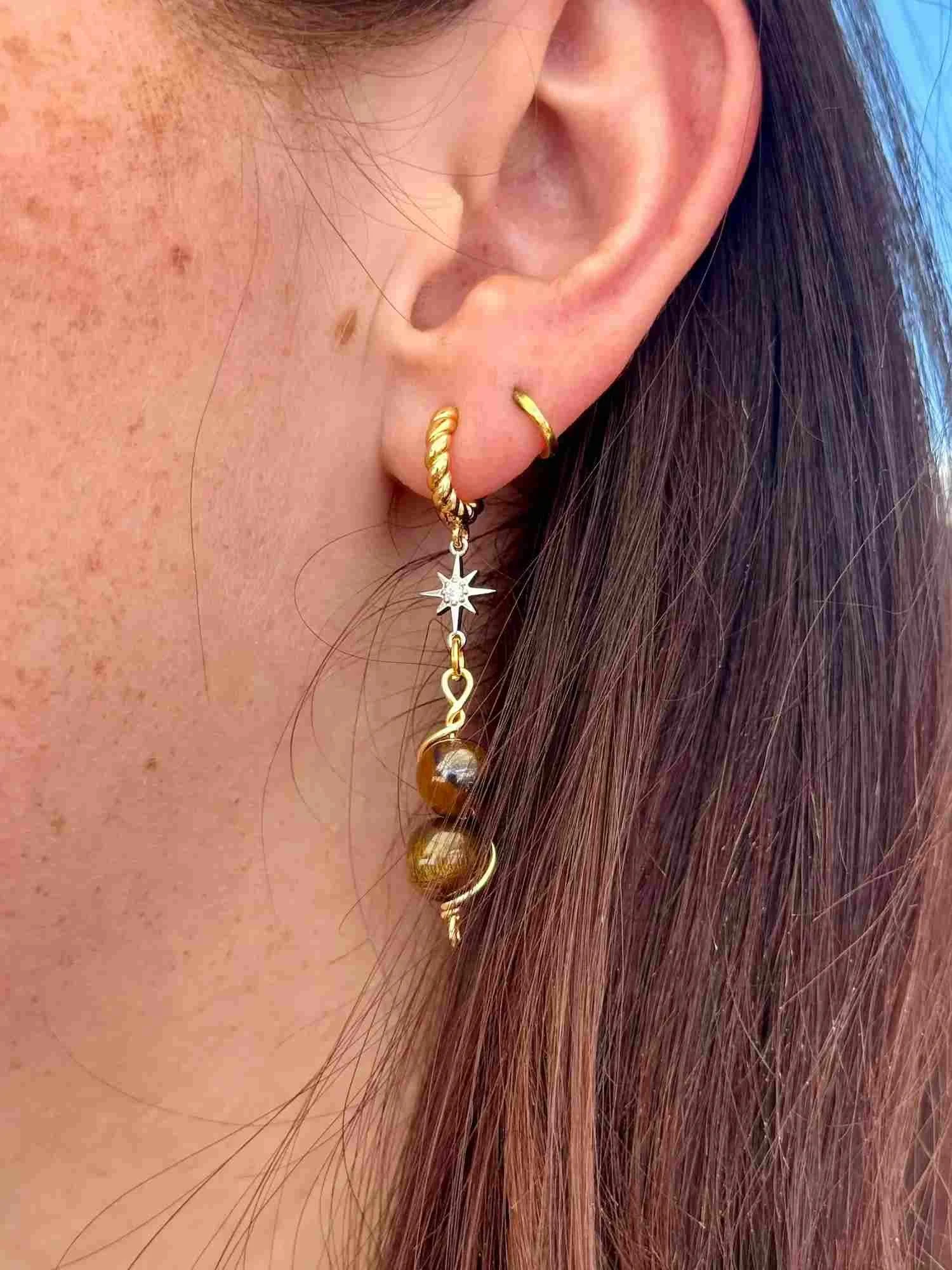 Close-up of an ear wearing a gold hoop earring with dangling bead charms