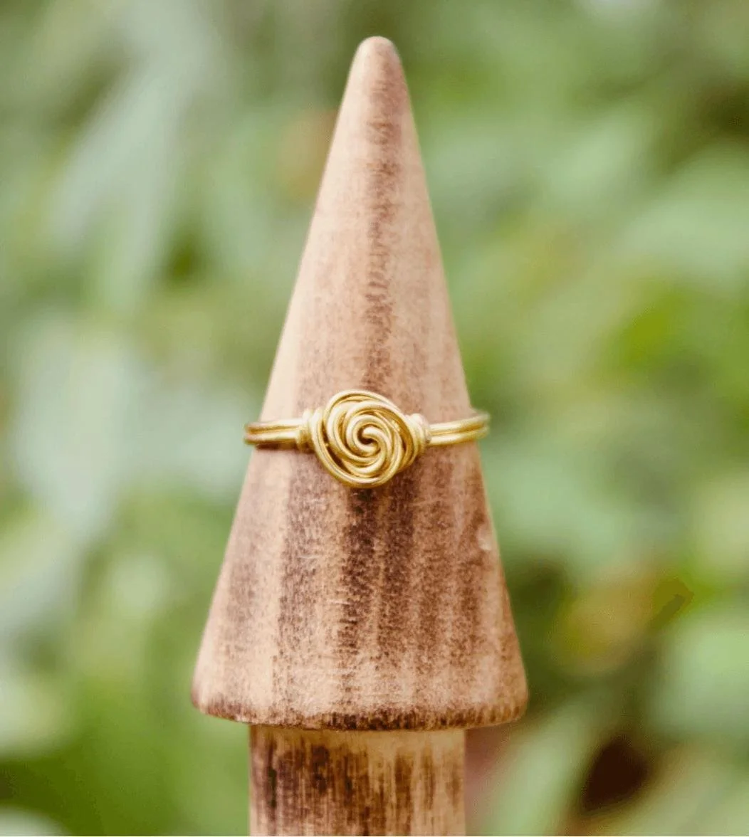 Gold ring with a swirl design displayed on a pointed wooden spike with a blurred green background.