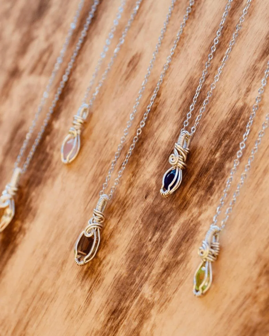 Several silver necklaces with wire-wrapped pendants hanging on a wooden display.