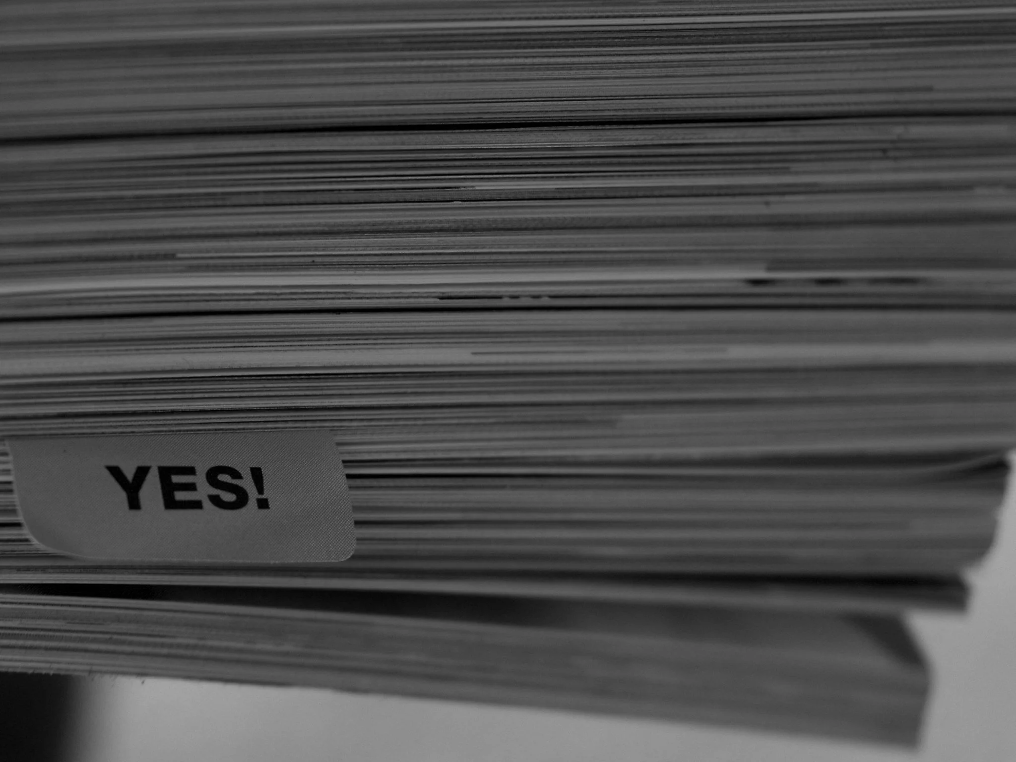 Close-up of a stack of papers or magazines with a partially visible sticker that reads 'YES!'