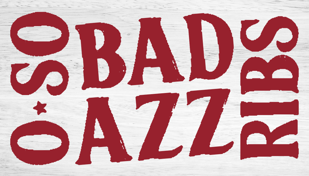 Wooden sign with white background and red text reading "SAO BADS AZZZIE" in a distressed font.