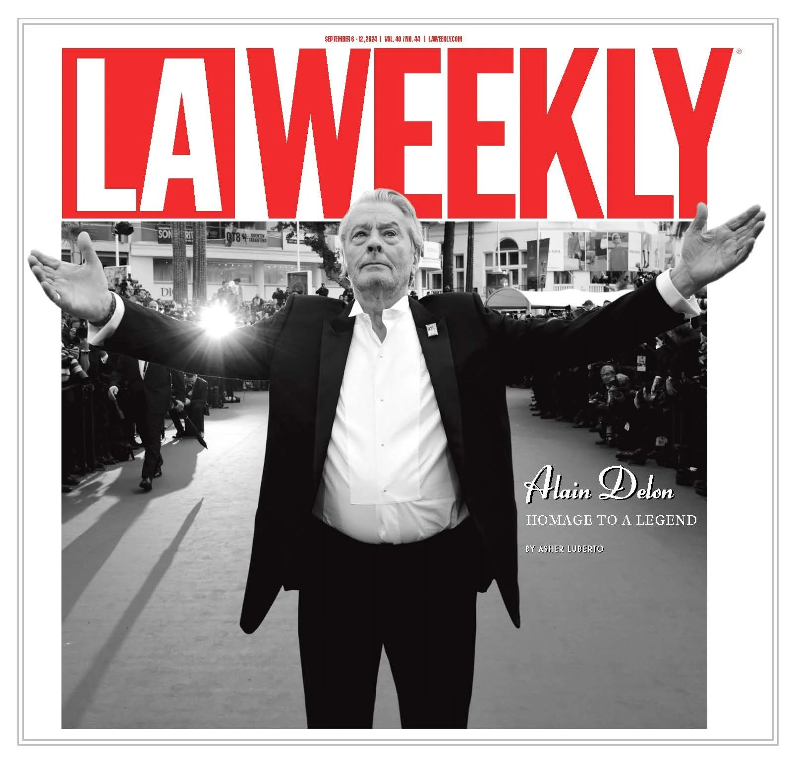 Cover of LA Weekly magazine featuring a black-and-white photograph of Alain Delon with arms outstretched, in an outdoor setting with a crowd. The title is in large red letters, and smaller text mentions the homage to a legend by Asher Luberto.