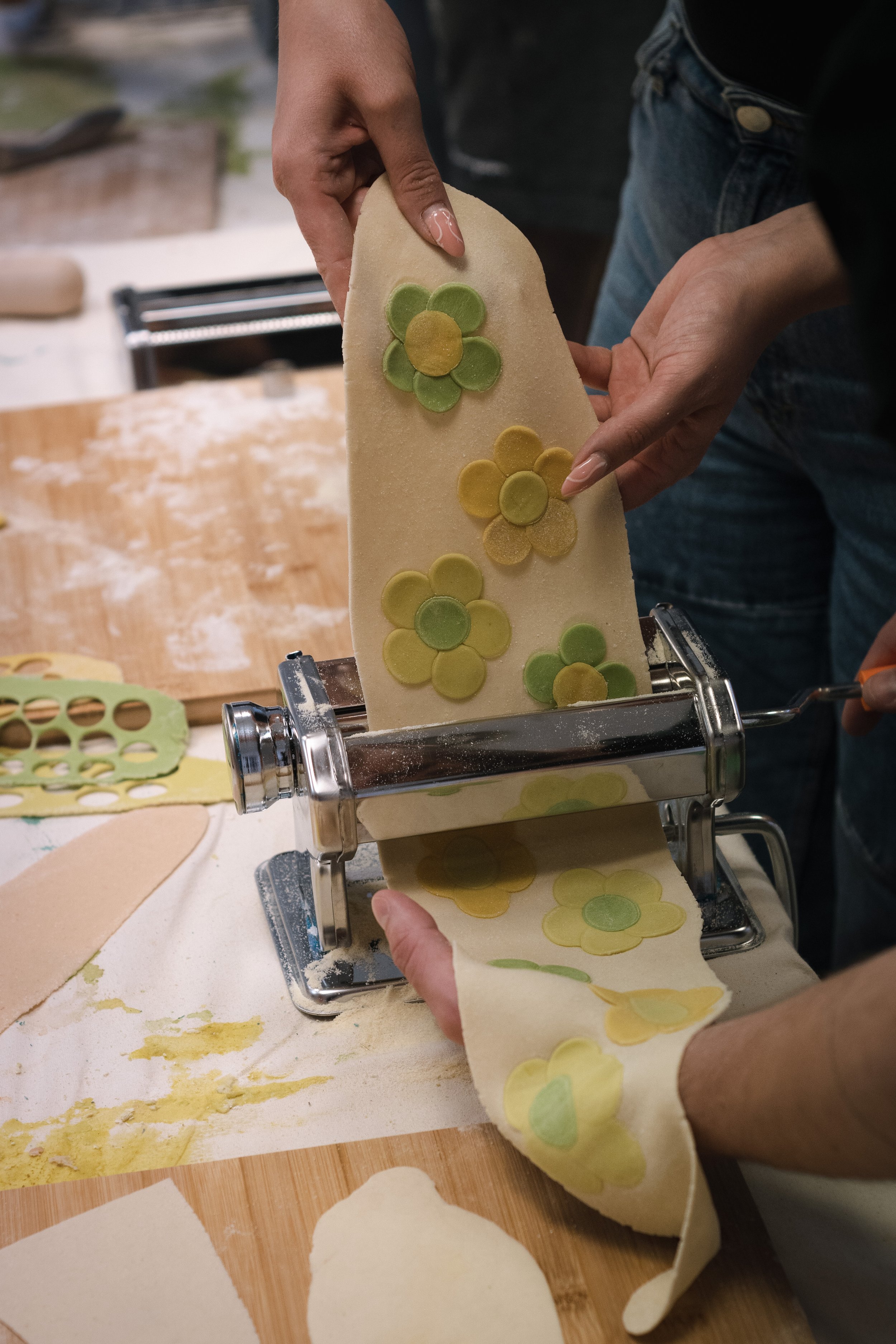 Person making pasta with floral patterns using a pasta machine.
