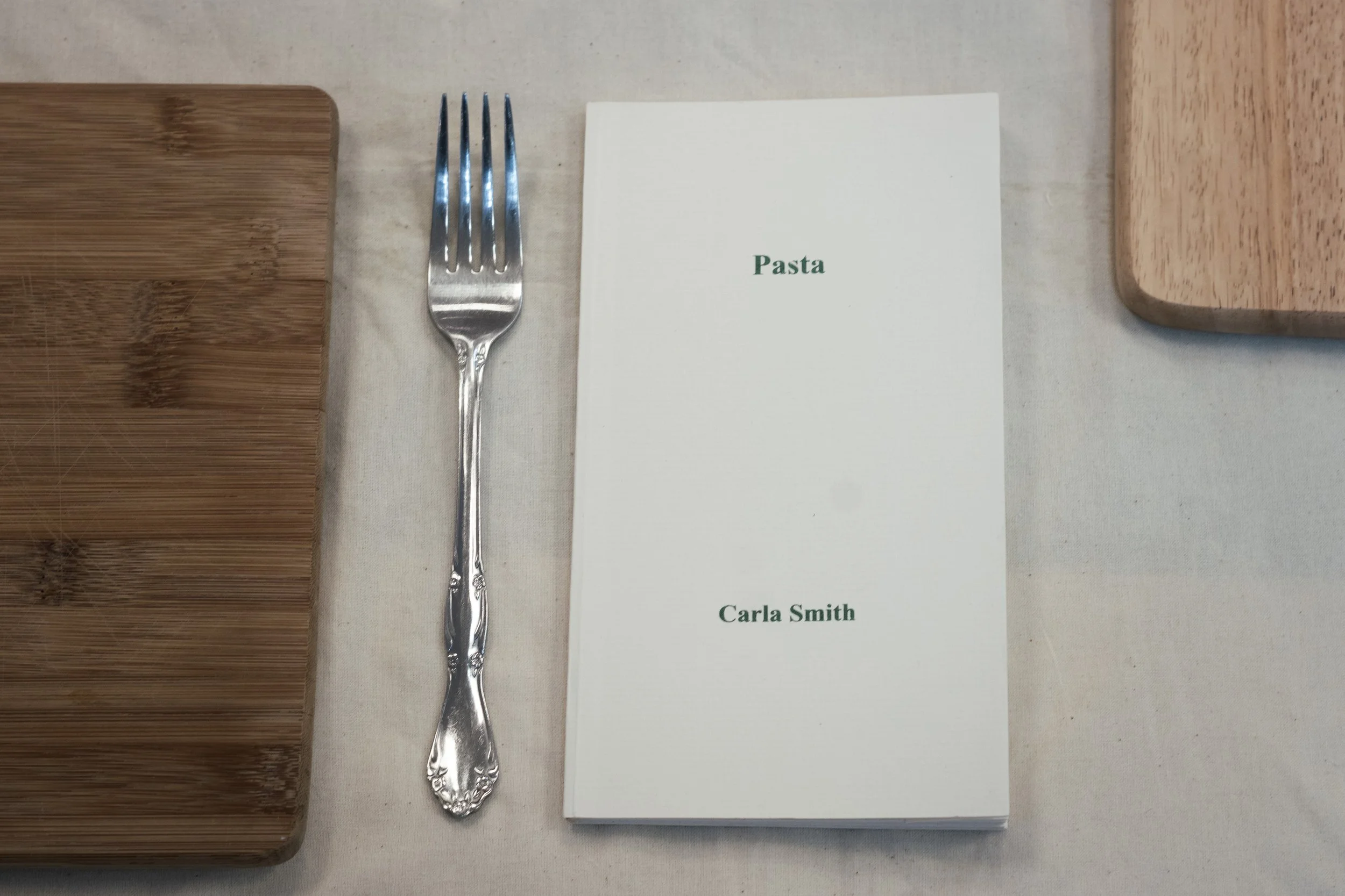 Fork next to a book titled "Pasta" by Carla Smith, on a table with wooden cutting boards.