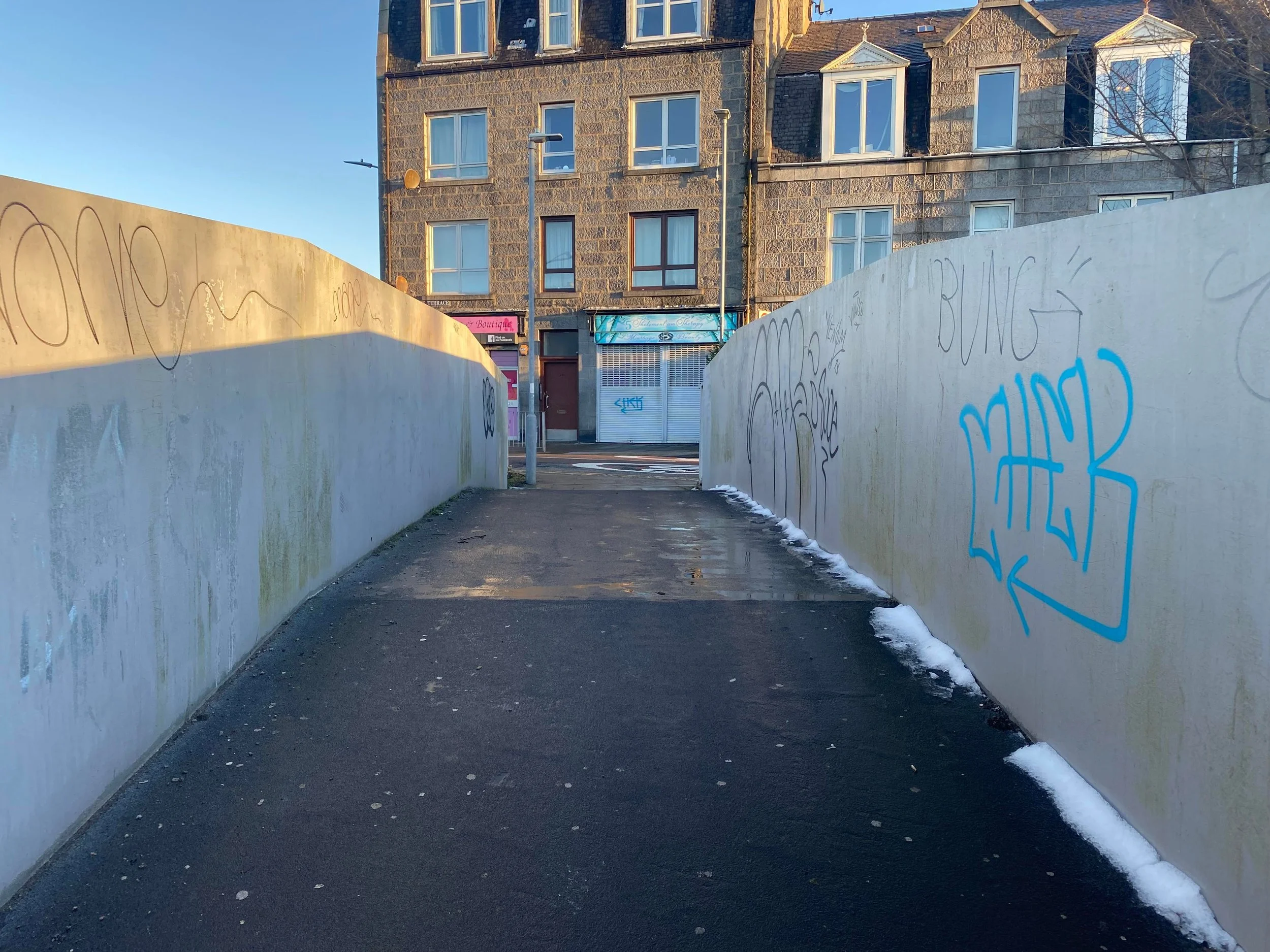 Urban walkway with graffiti on concrete walls and a building in the background.