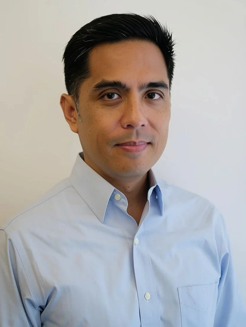 Professional headshot of a man in a dark suit and light blue dress shirt against a gray background.