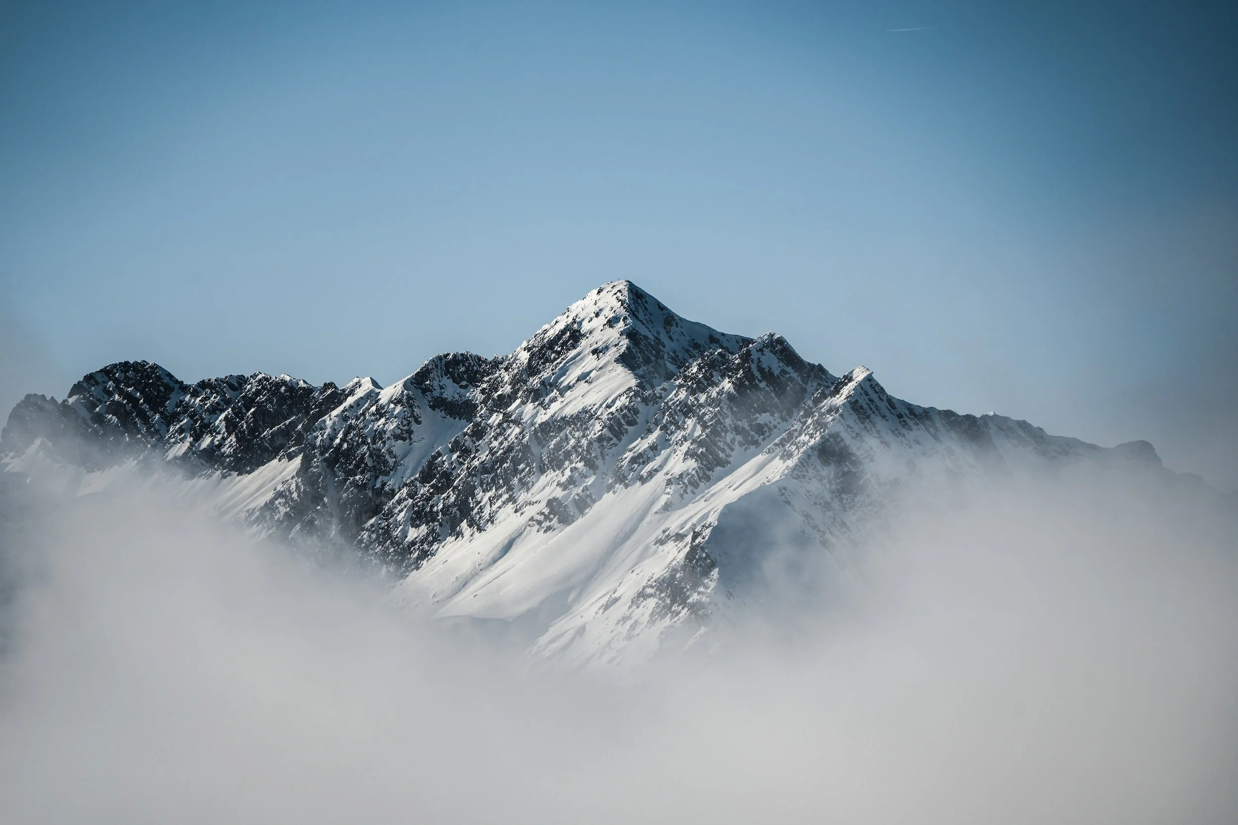 Snow-covered mountain peaks rising above a layer of clouds with a clear blue sky above.