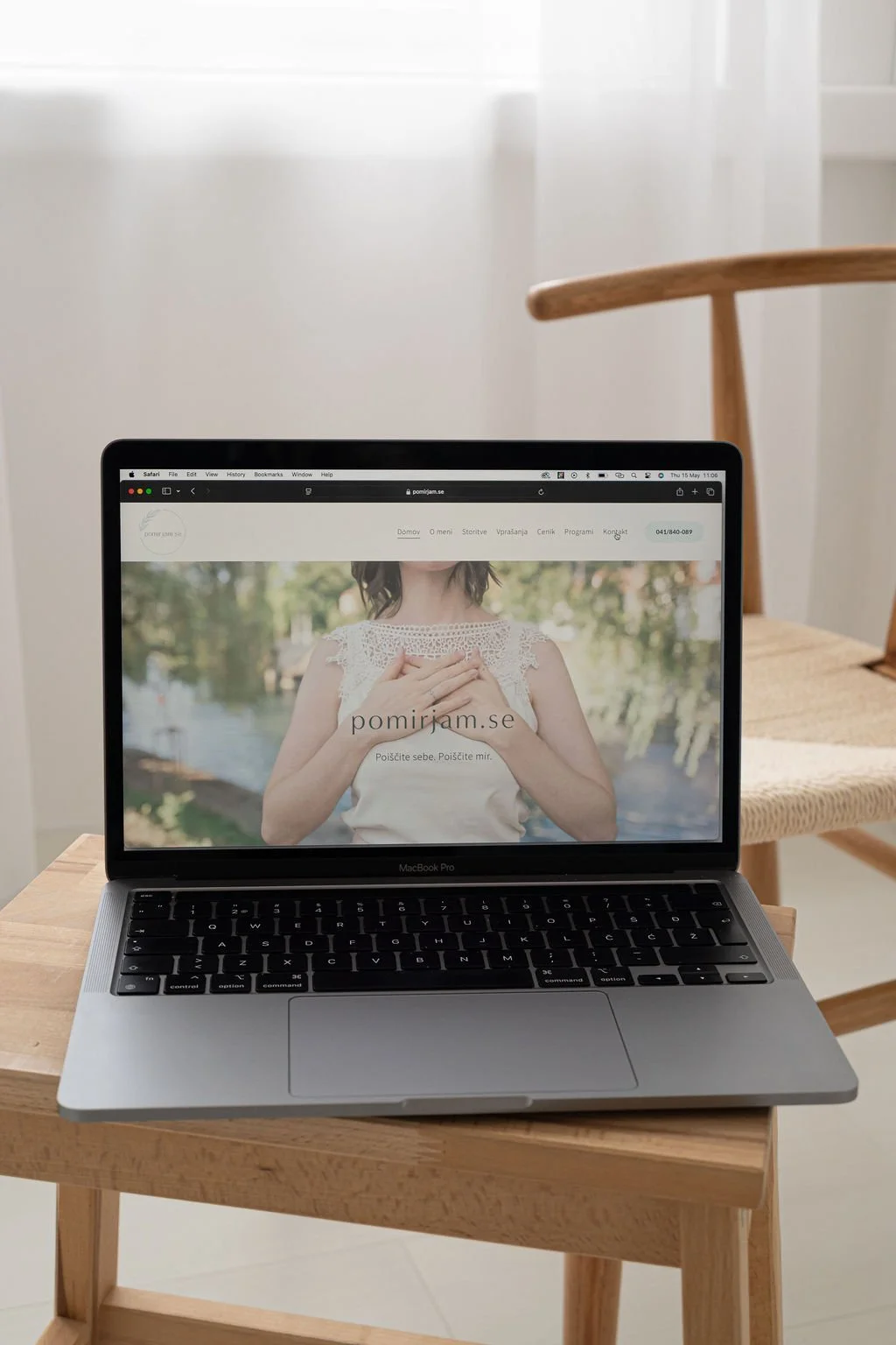 Open MacBook Pro placed on a wooden table displaying a website 'pomijam.se' featuring a person with hands over their chest, outdoors.