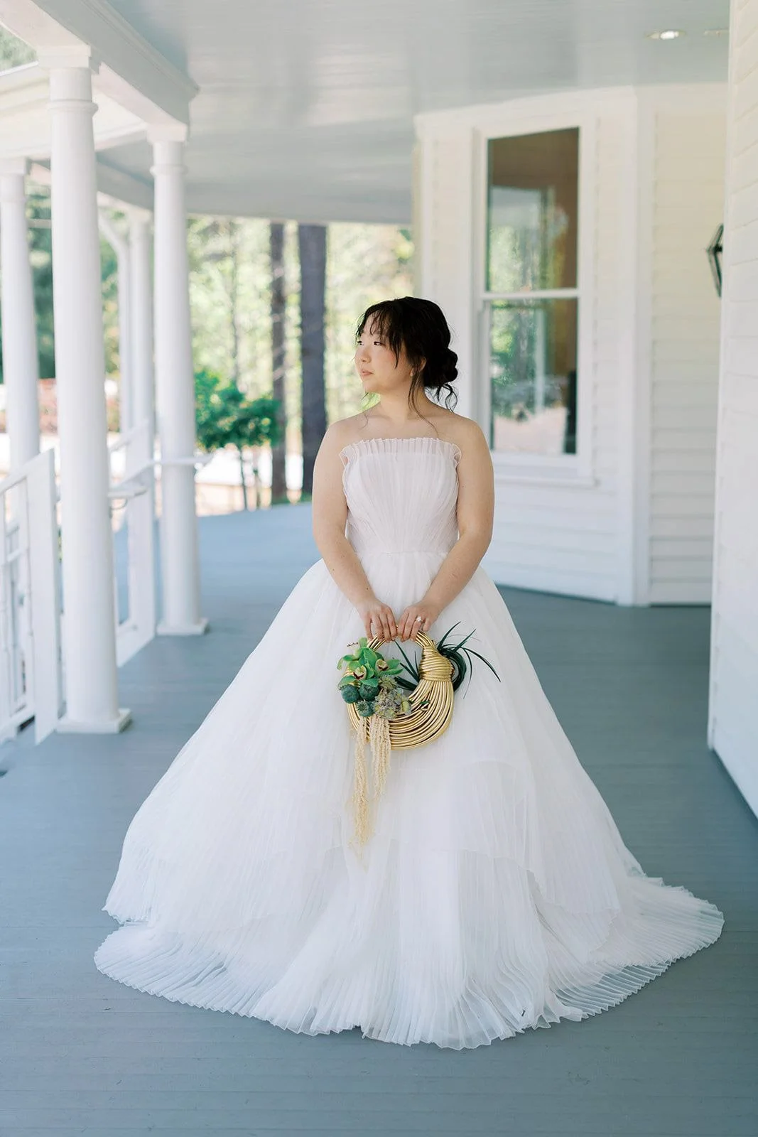 A bride stands on the porch at The Upchurch wedding venue holding a modern floral bouquet designed by Wild Flora Flowers in Raleigh, North Carolina.