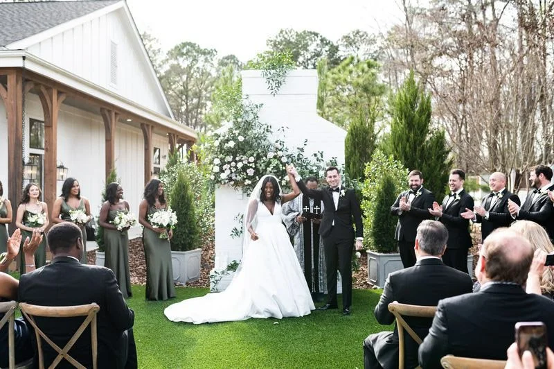 Wedding ceremony at The Bradford with floral design by Wild Flora Flowers, featuring the couple celebrating under a white brick fireplace with lush greenery and ceremony florals.