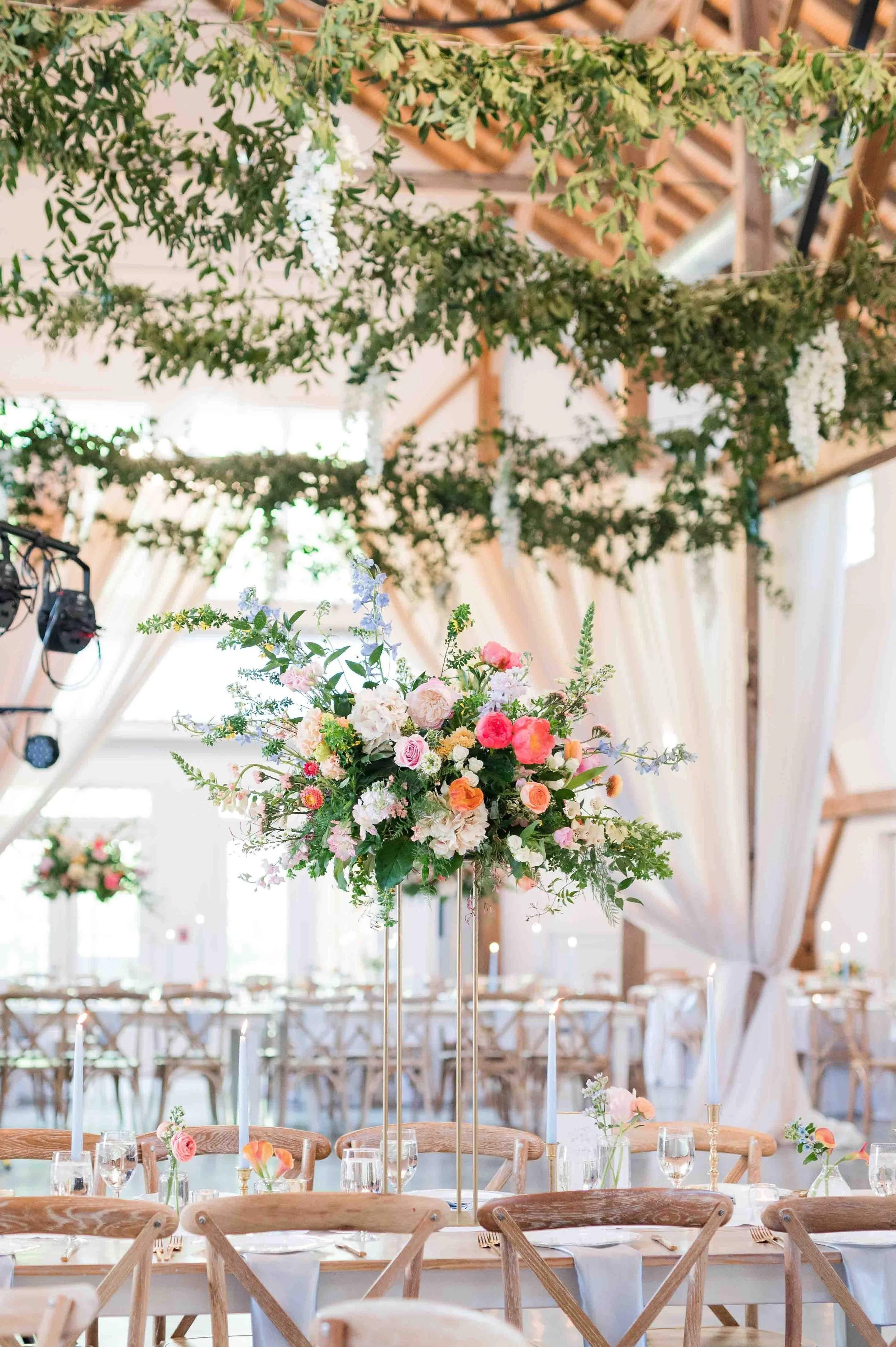 Elevated floral centerpiece on a reception table beneath hanging greenery and draped fabric at a wedding at The Barn of Chapel Hill
