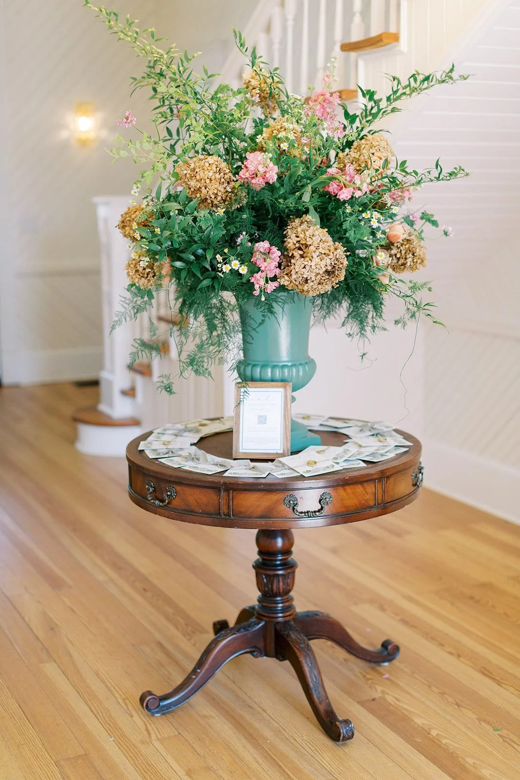 A large, natural floral arrangement by Wild Flora Flowers displayed on an entry table at The Upchurch wedding venue, featuring seasonal blooms and lush greenery.