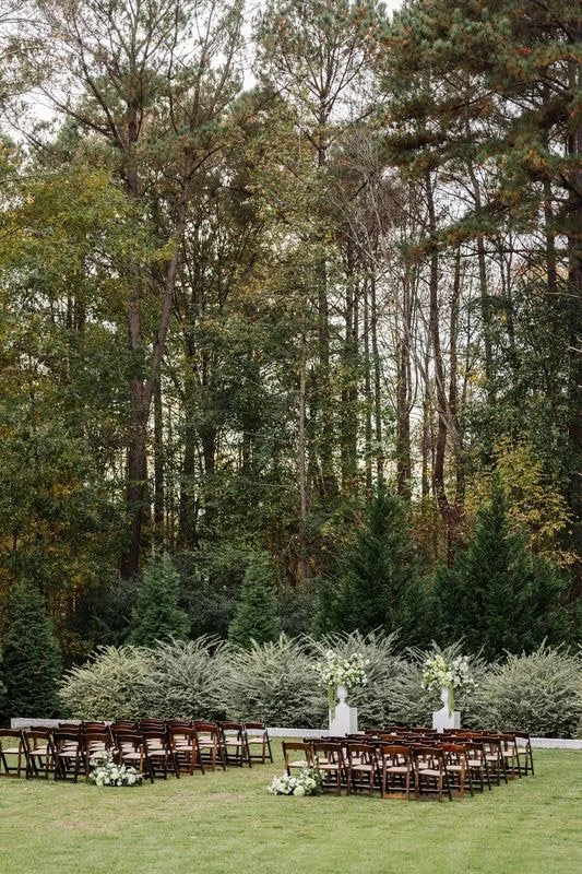 Outdoor wedding ceremony at The Bradford with wooden chairs and aisle floral arrangements designed by Wild Flora Flowers.