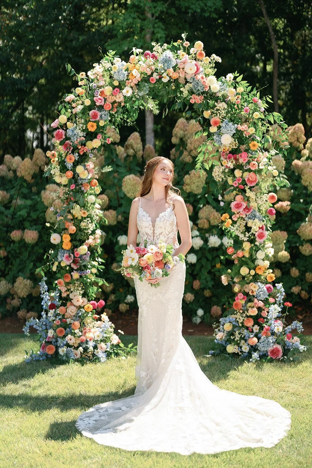 Bride standing beneath a colorful circular floral arch during a wedding at The Barn of Chapel Hill