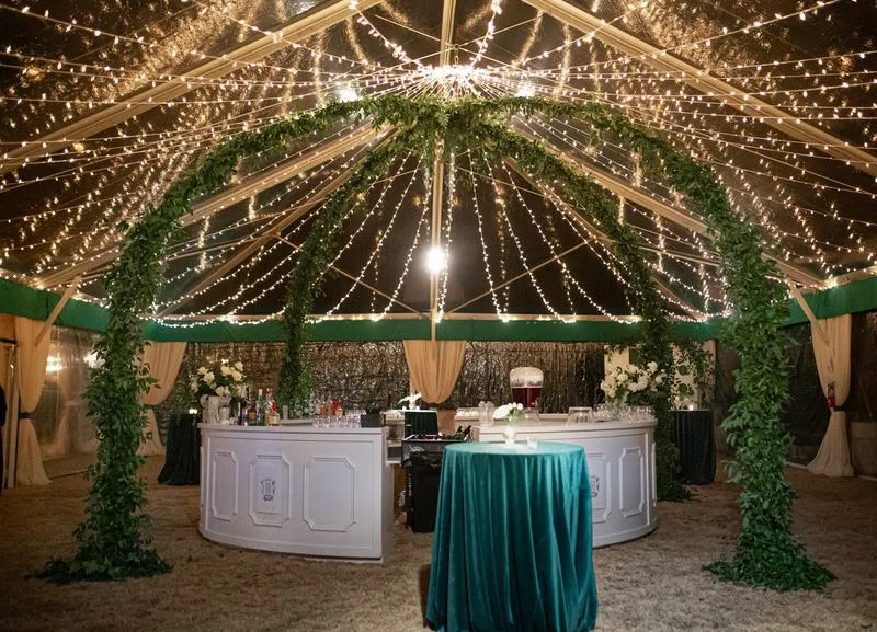 Wedding reception bar under a tented canopy with cascading string lights and greenery arches at The Barn of Chapel Hill