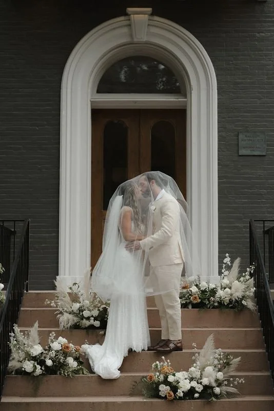 Couple sharing a quiet moment on the front steps of Heights House in Raleigh, framed by soft ceremony florals and historic architecture