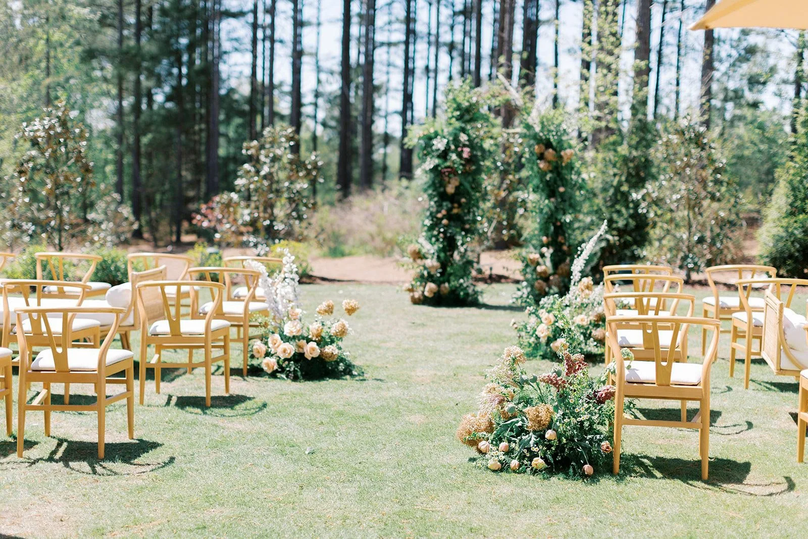 A garden ceremony setup with wooden chairs and aisle florals designed by Wild Flora Flowers at The Upchurch wedding venue in Raleigh, North Carolina.