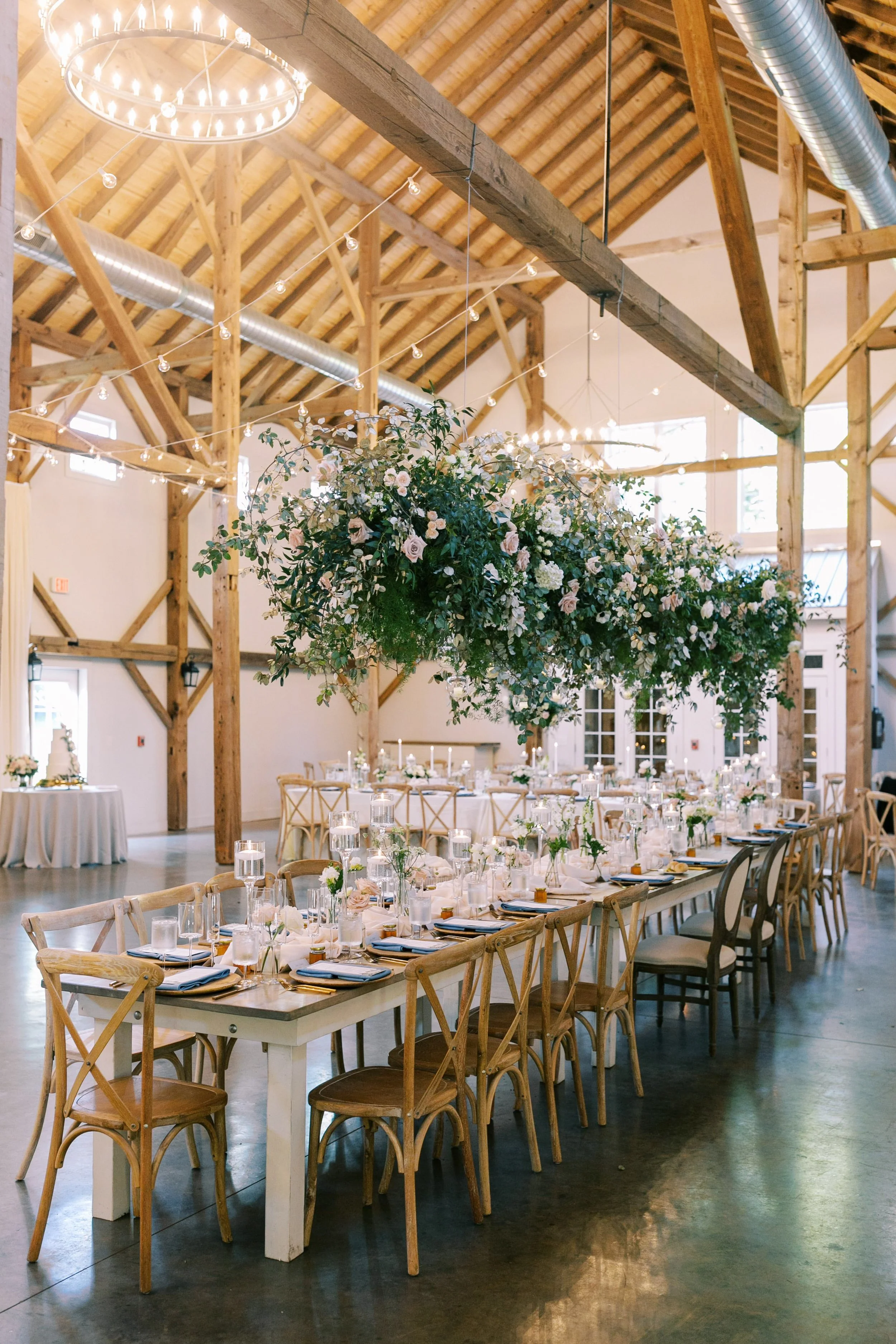 Long reception tables styled with candles and place settings beneath a hanging greenery installation at a wedding at The Barn of Chapel Hill