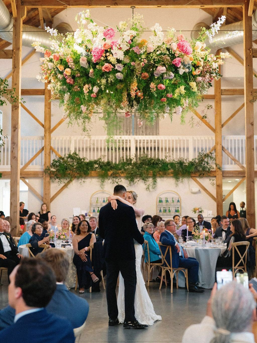 Couple sharing their first dance beneath a lush hanging floral installation at a wedding reception at The Barn of Chapel Hill
