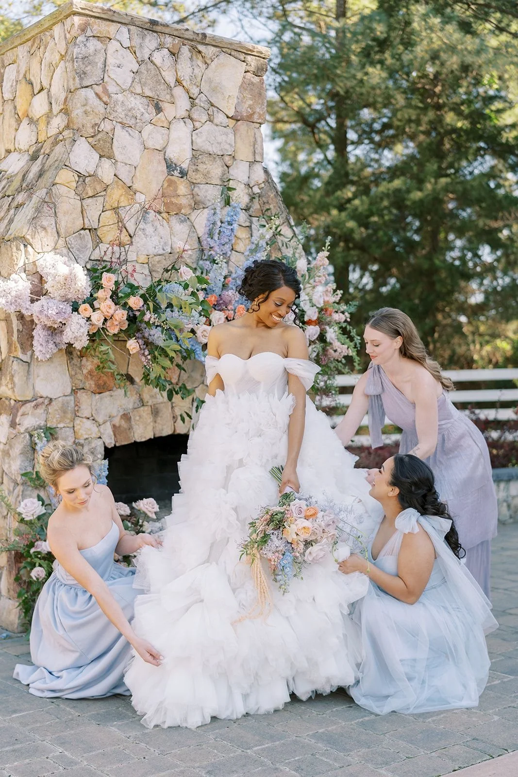 Bride and bridesmaids standing by a fireplace decorated with pastel floral arrangements in a romantic wedding setting