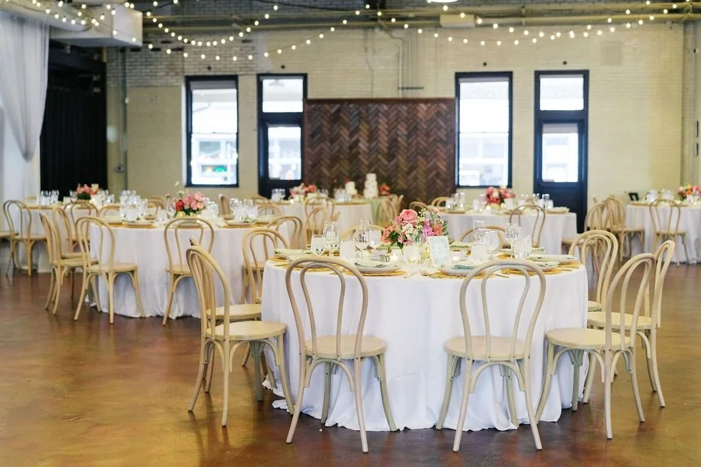 Wedding reception setup at Traine in Raleigh with round tables, bentwood chairs, soft string lighting, and floral centerpieces
