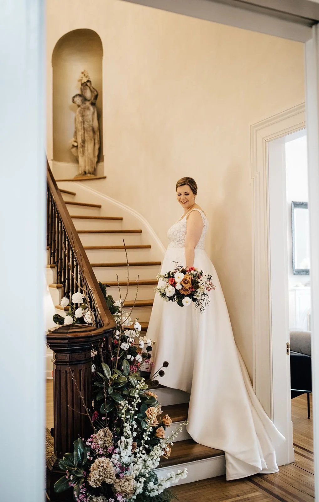 Bride standing on the staircase at Merrimon Wynne House in Raleigh, surrounded by soft garden-style wedding florals and historic interior details