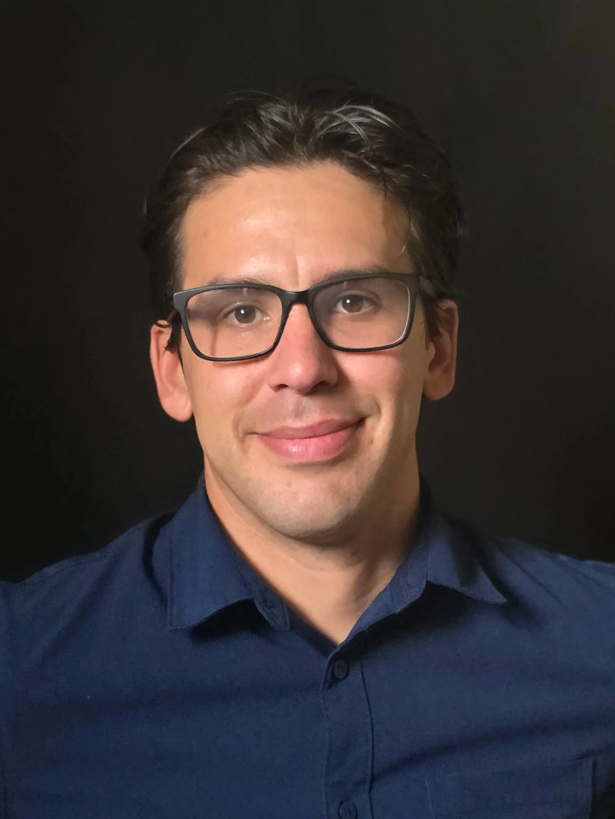 Man wearing blue collared shirt and eyeglasses smiling at the camera