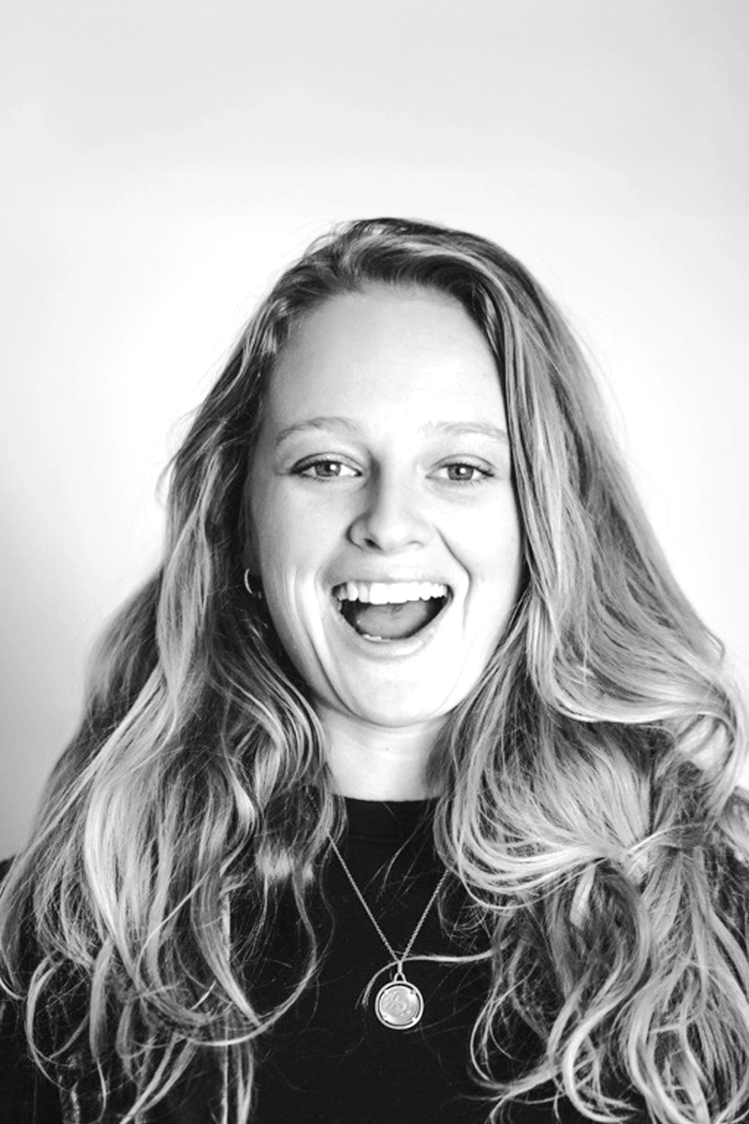 Black and white photo of a young woman with long, wavy hair smiling and showing her teeth.