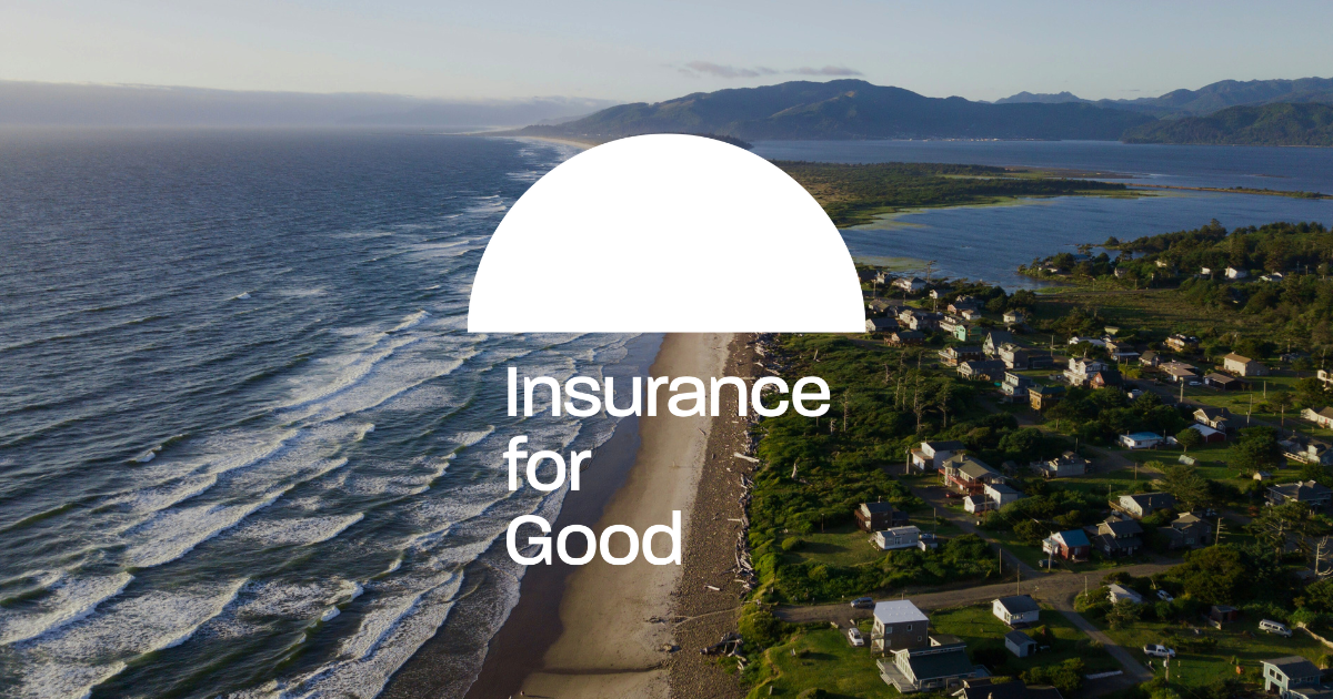 Aerial view of a coastline with waves hitting the beach, residential houses, green trees, and mountains in the background under a clear sky. Insurance for Good logo.