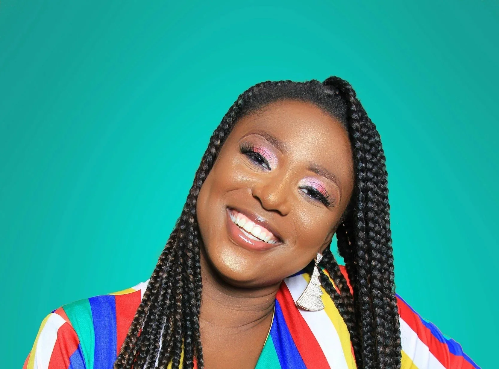 Woman with dark braided hair smiles against a turquoise background, wearing colorful clothing and large earrings.