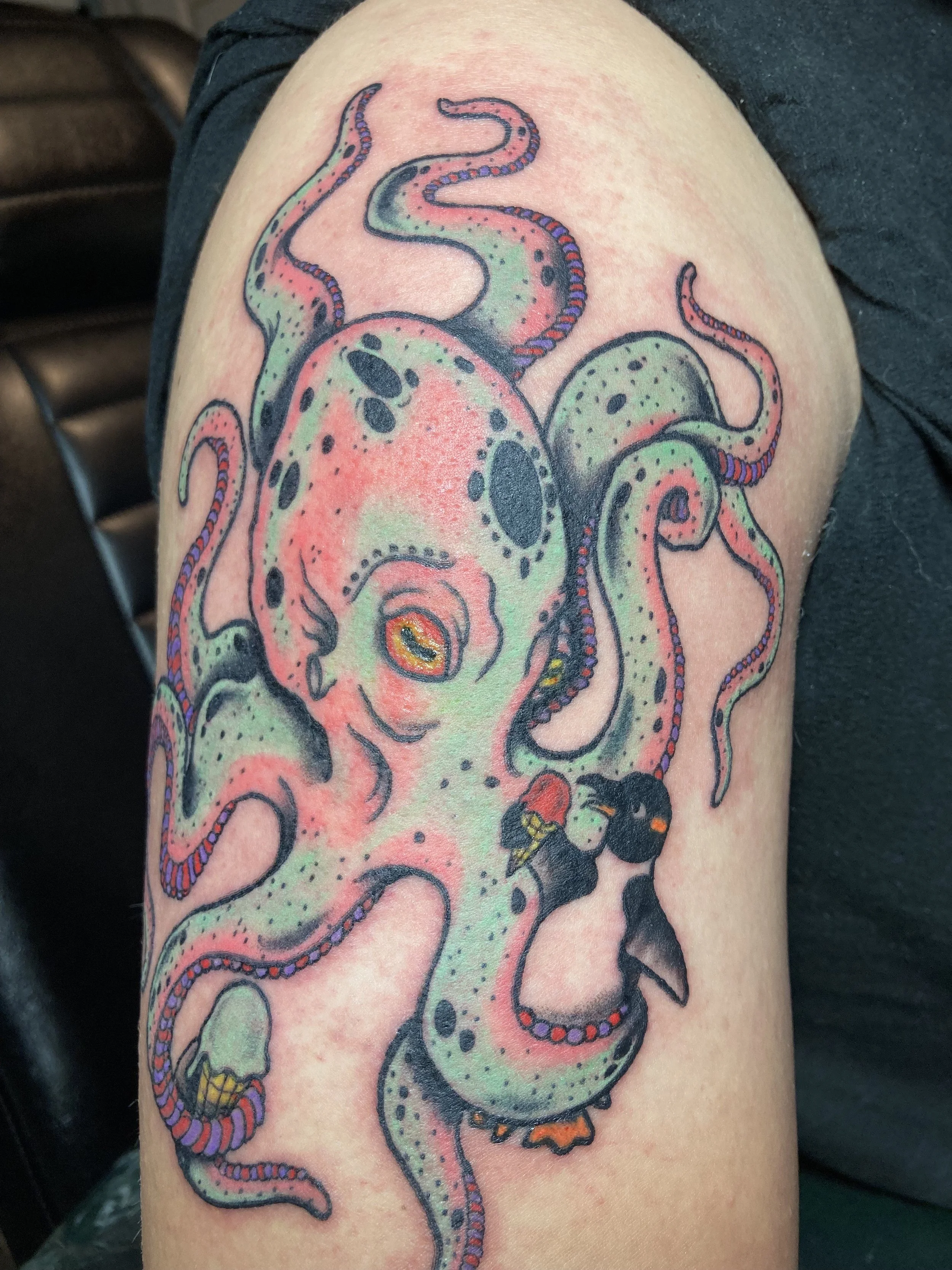 Colorful tattoo of a pink and green octopus holding a black and orange penguin on someone's arm.