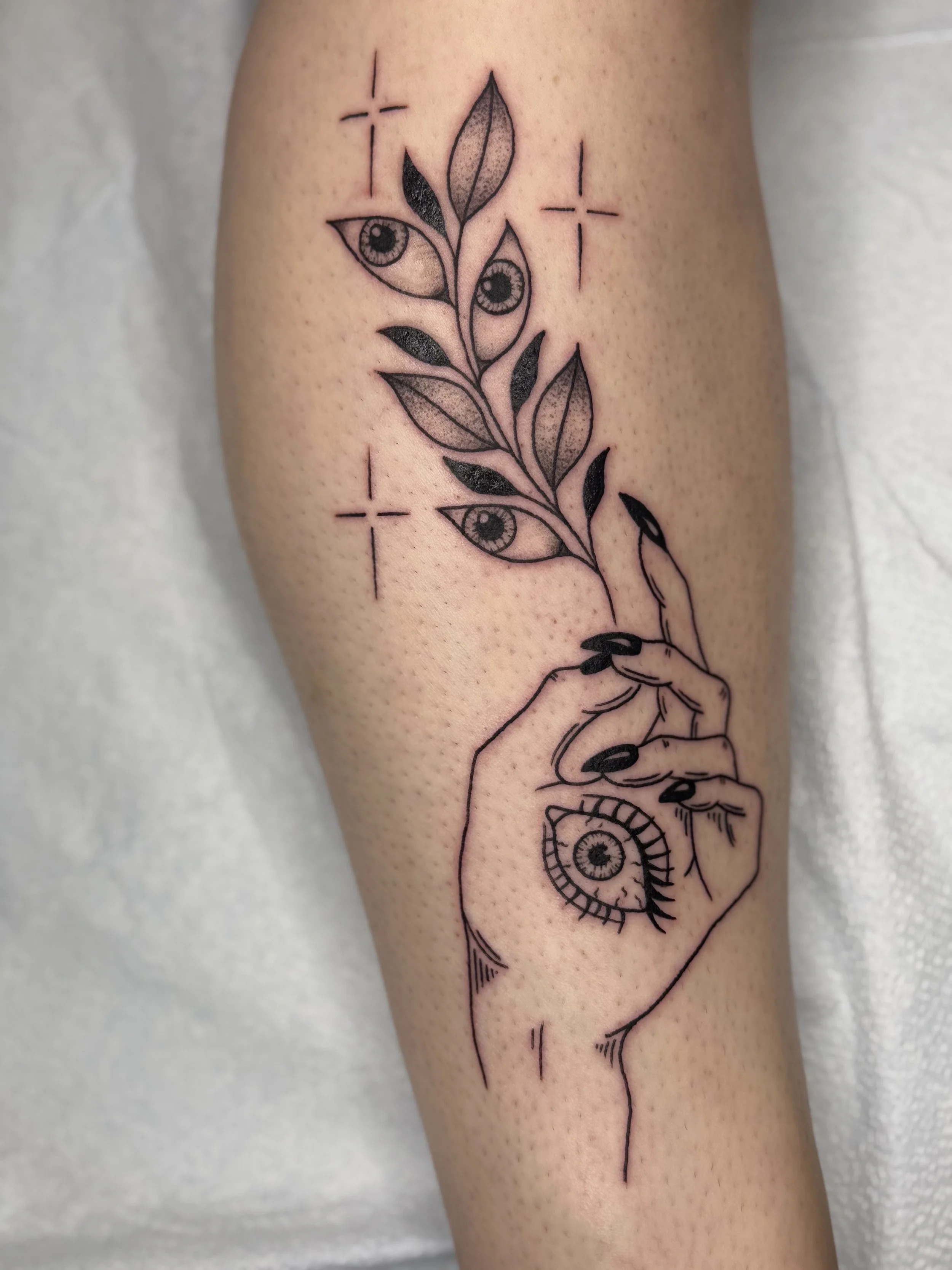 Tattoo of a hand holding a stem with leaves and eyes, with two small crosses nearby.