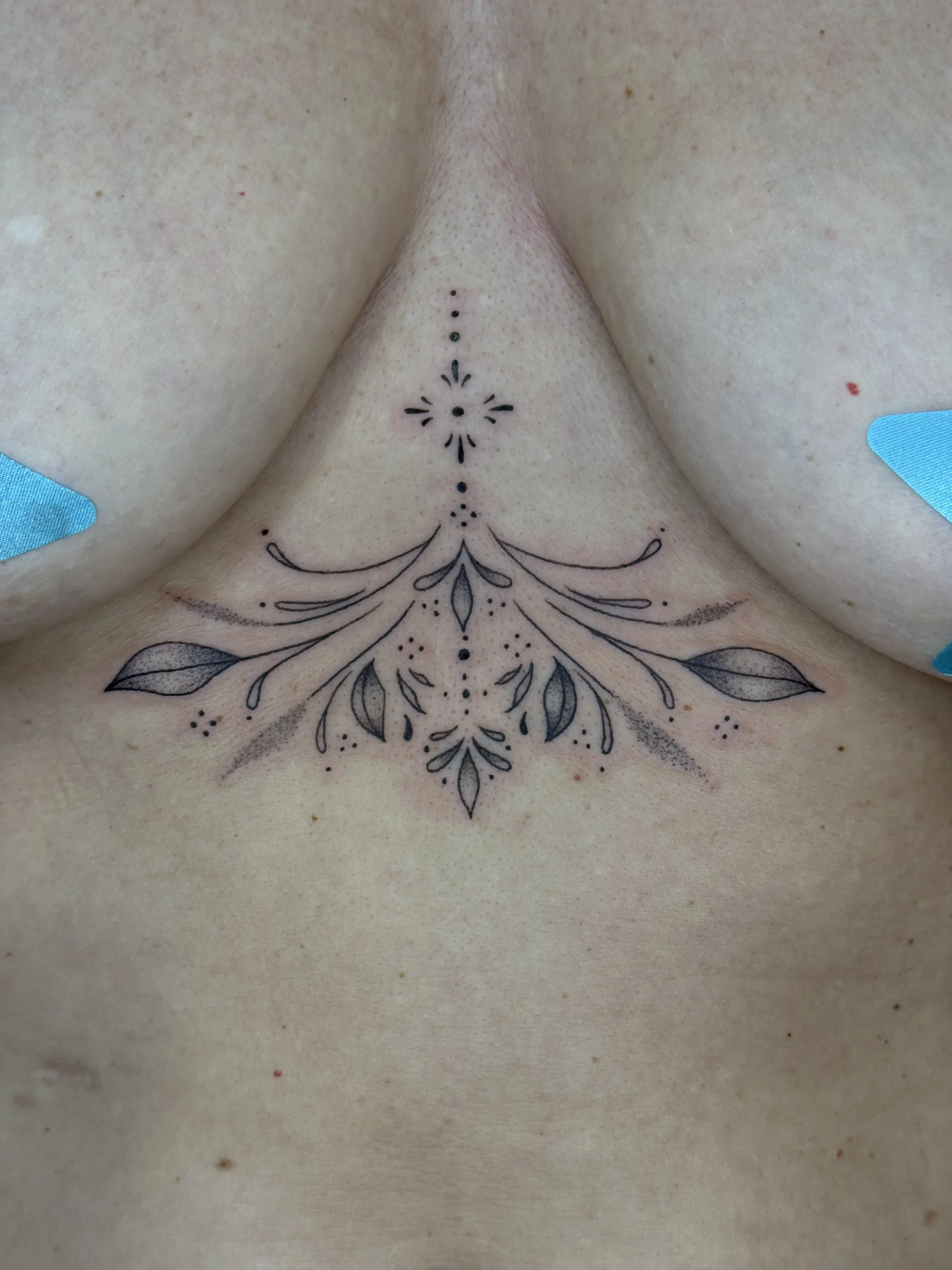 Close-up of a decorative tattoo under a person's collarbone with floral and geometric patterns.