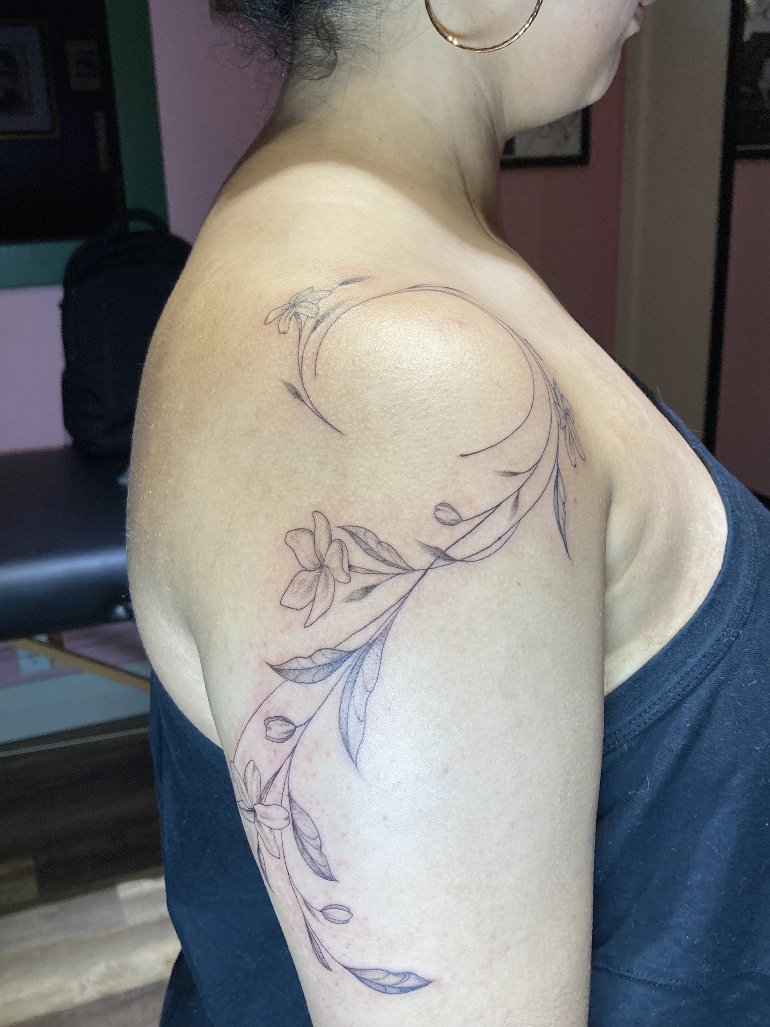A woman with a floral tattoo on her shoulder and upper arm, wearing earrings and a dark shirt.