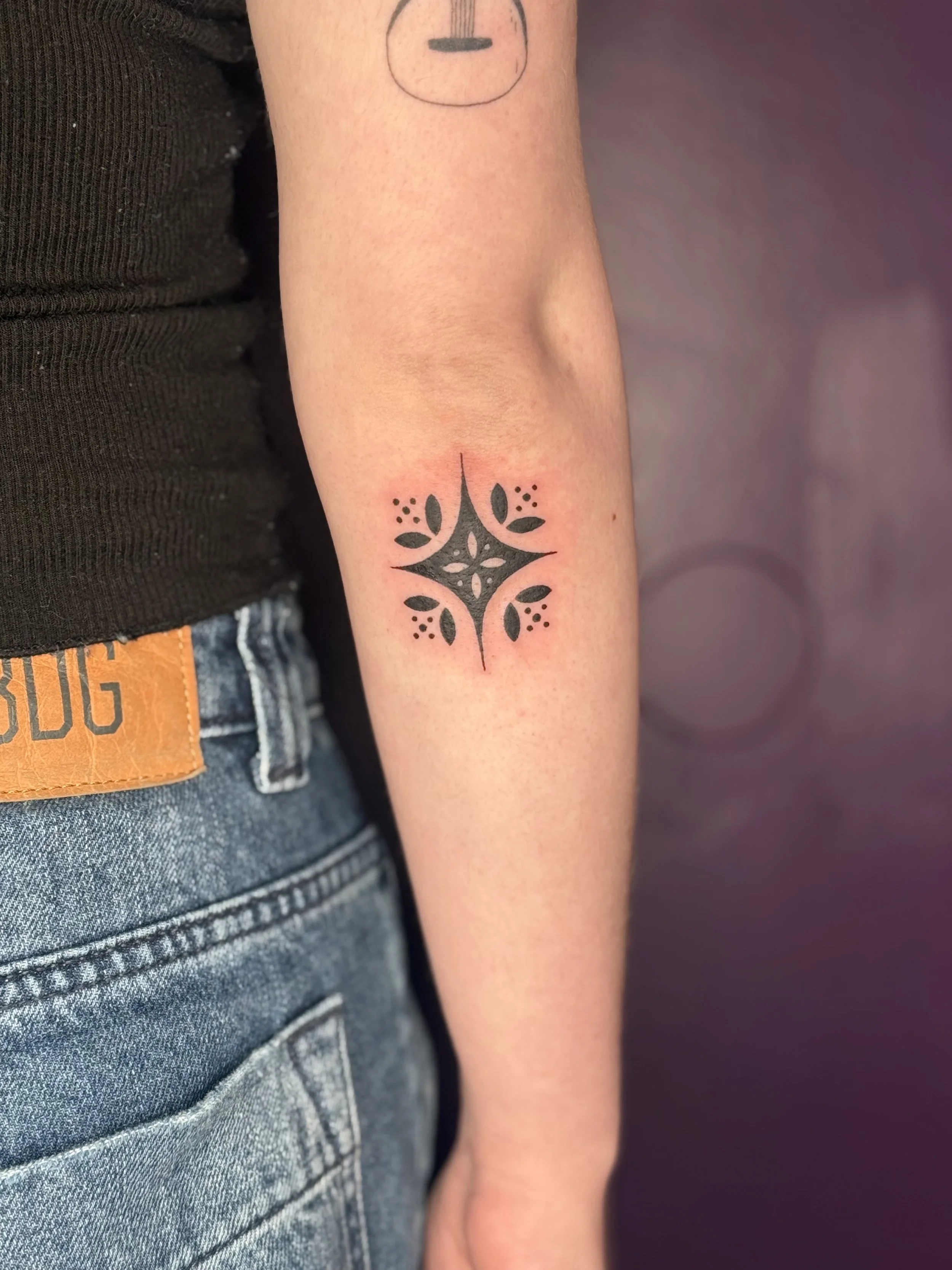 Tattoo of a black geometric and floral design on a person's forearm.