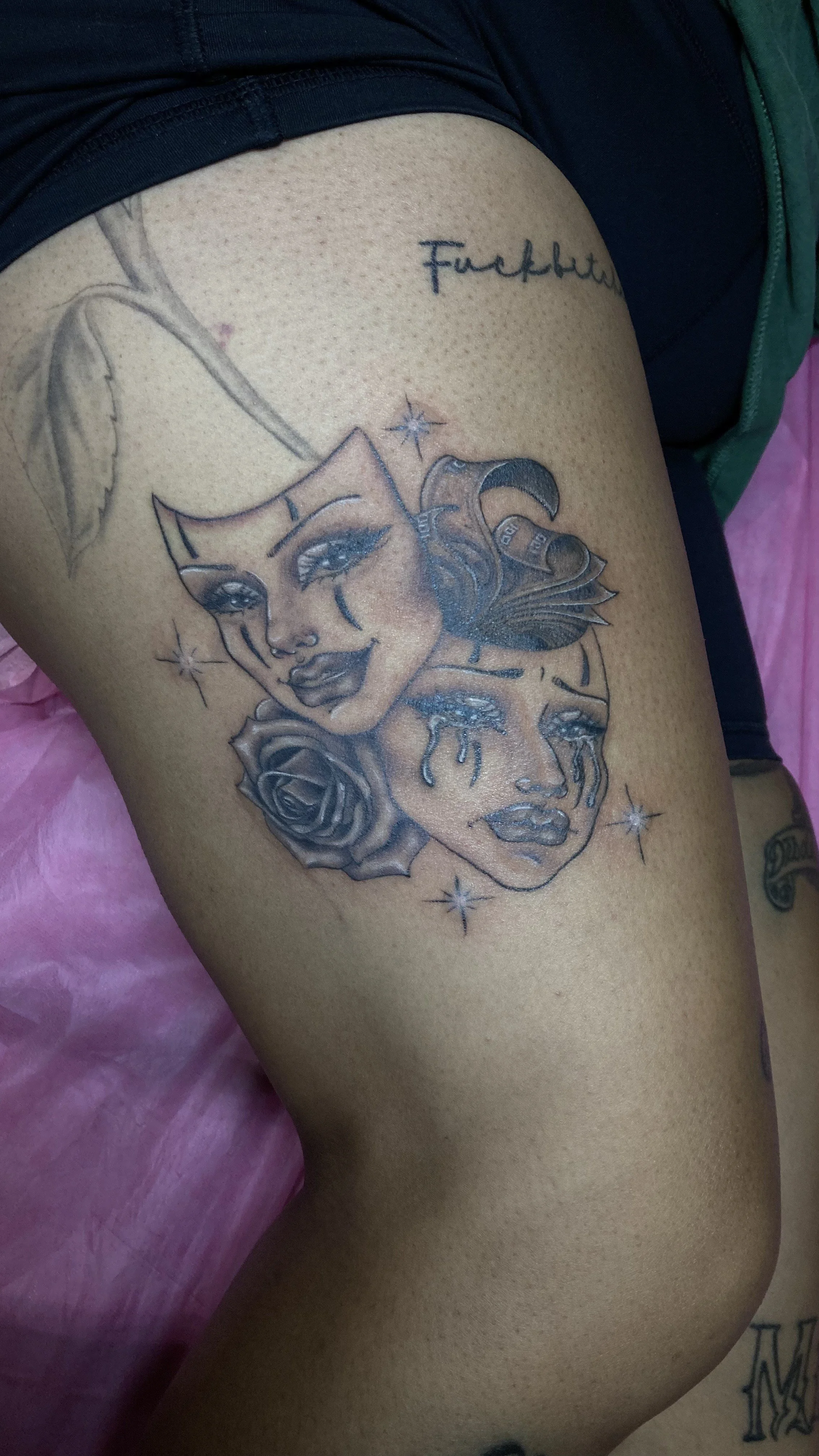 Tattoo of two women's faces, one with makeup and a star near her eye, the other with tears and a rose below her chin, surrounded by stars and leaves.