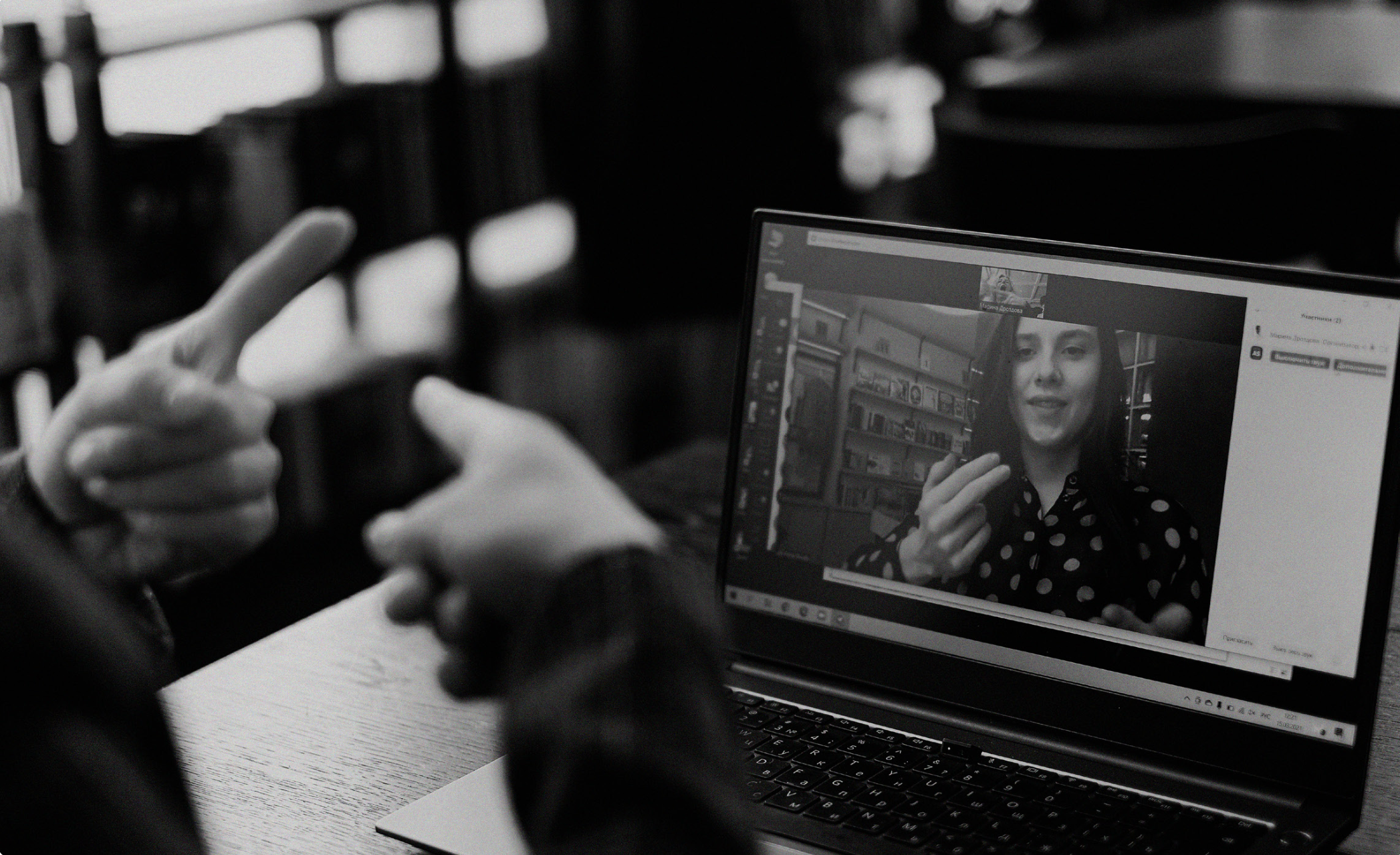 A person off camera uses sign language to communicate with someone during a video meeting using a laptop.