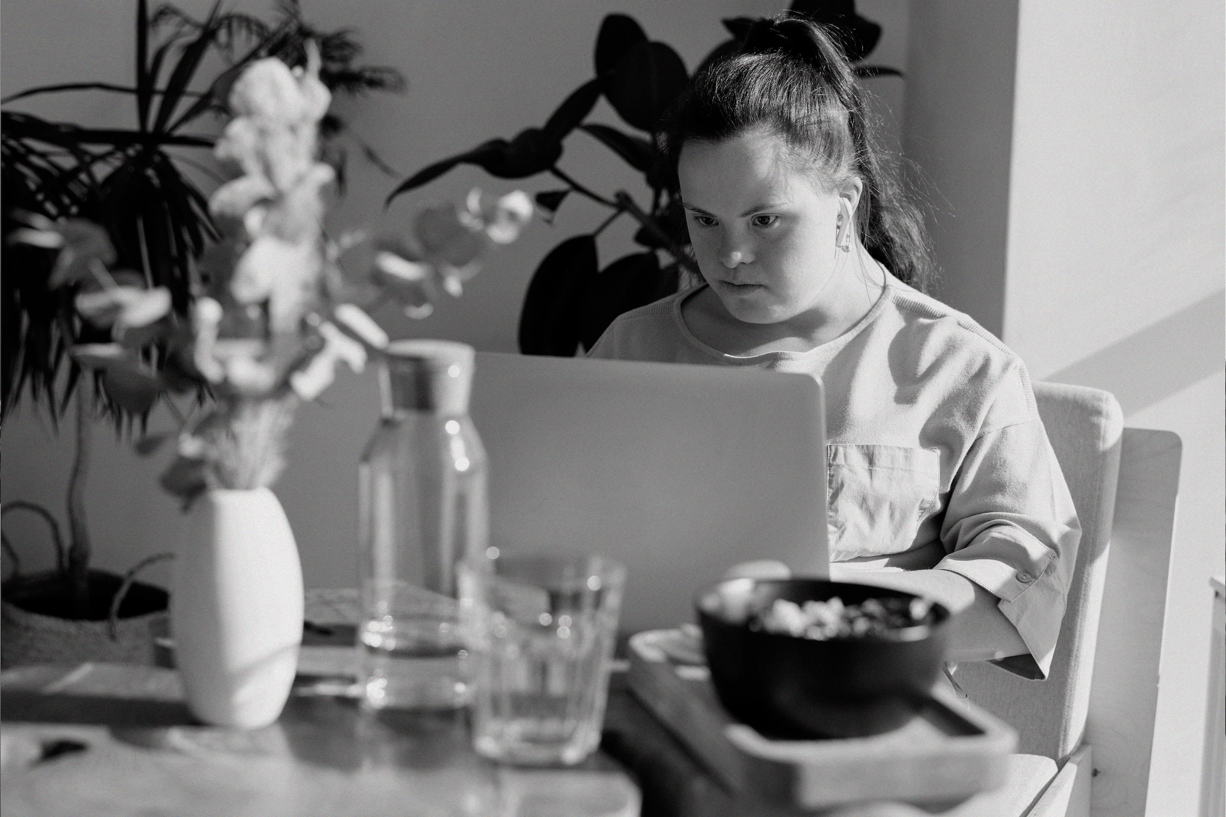 A person sits at a table in a sunny room working on a laptop computer.