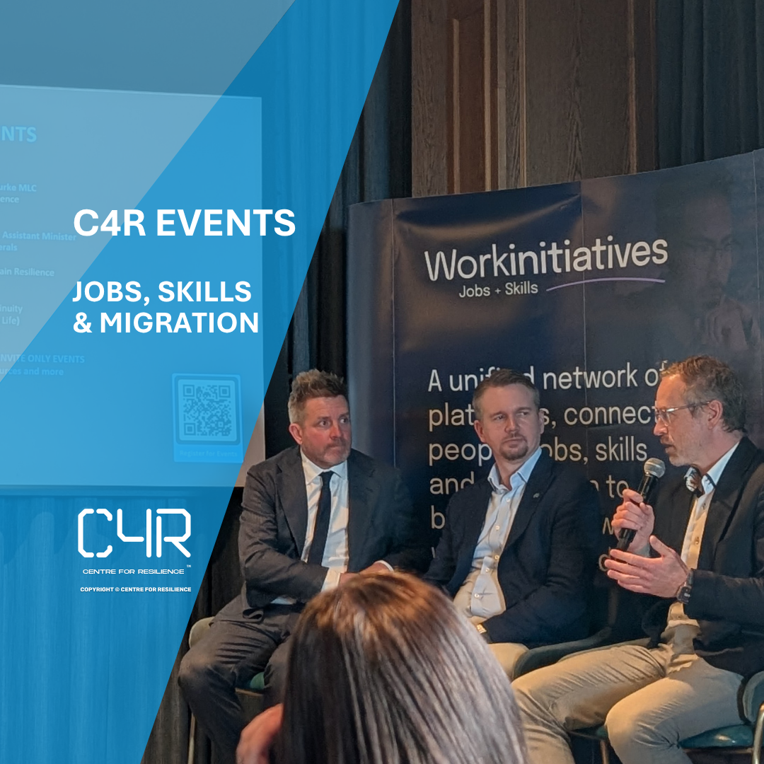 Panel discussion at a CAR Events event focused on jobs, skills, and migration, with four men in suits seated on stage, one speaking into a microphone, with a large banner behind them displaying "Workinitiatives" and related text.
