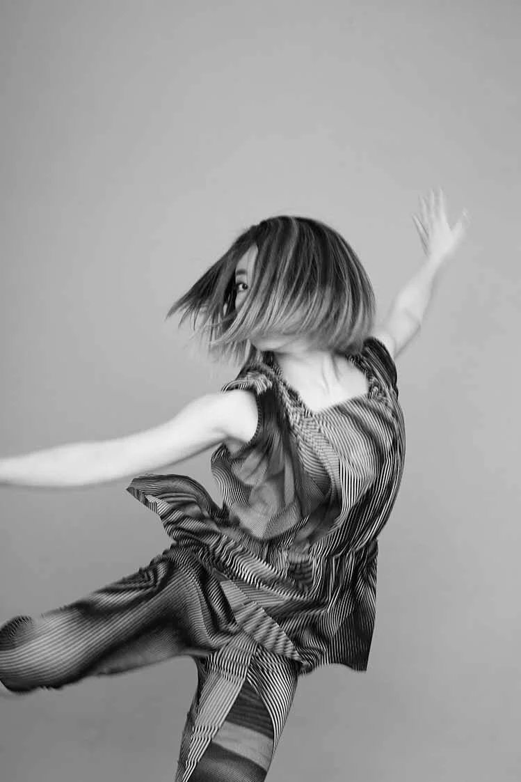 グレースケールの写真で、髪を振り乱して踊っている女性の姿。背景は単色の壁。