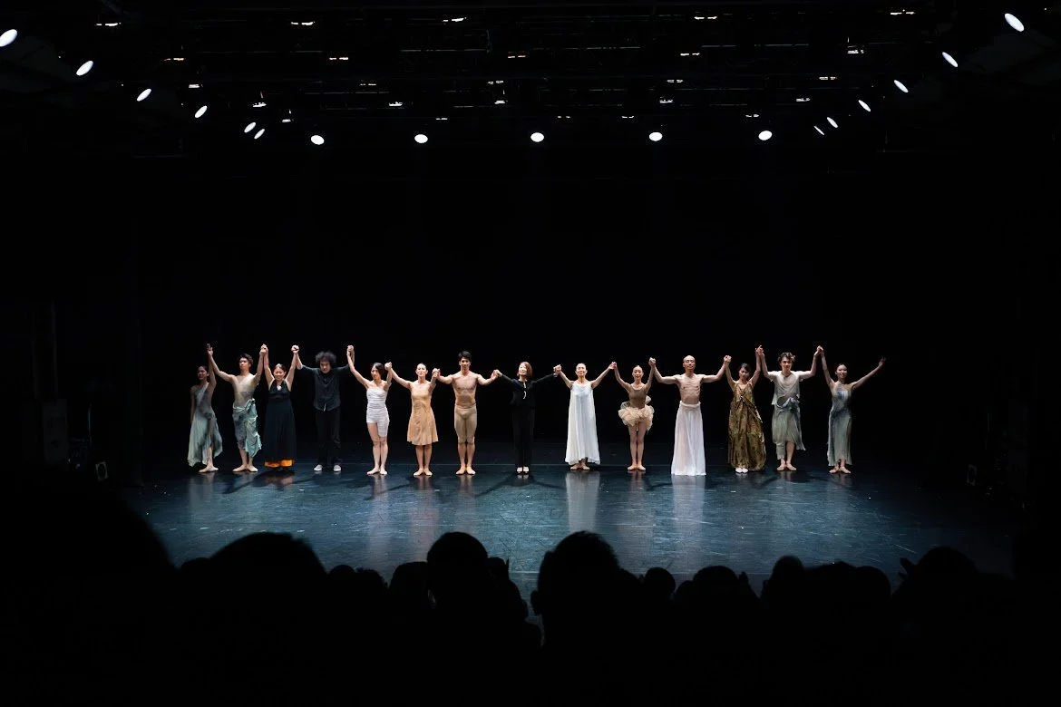 舞台で観客に向かって手をつなぐダンサーのグループ。夜の公演の舞台。