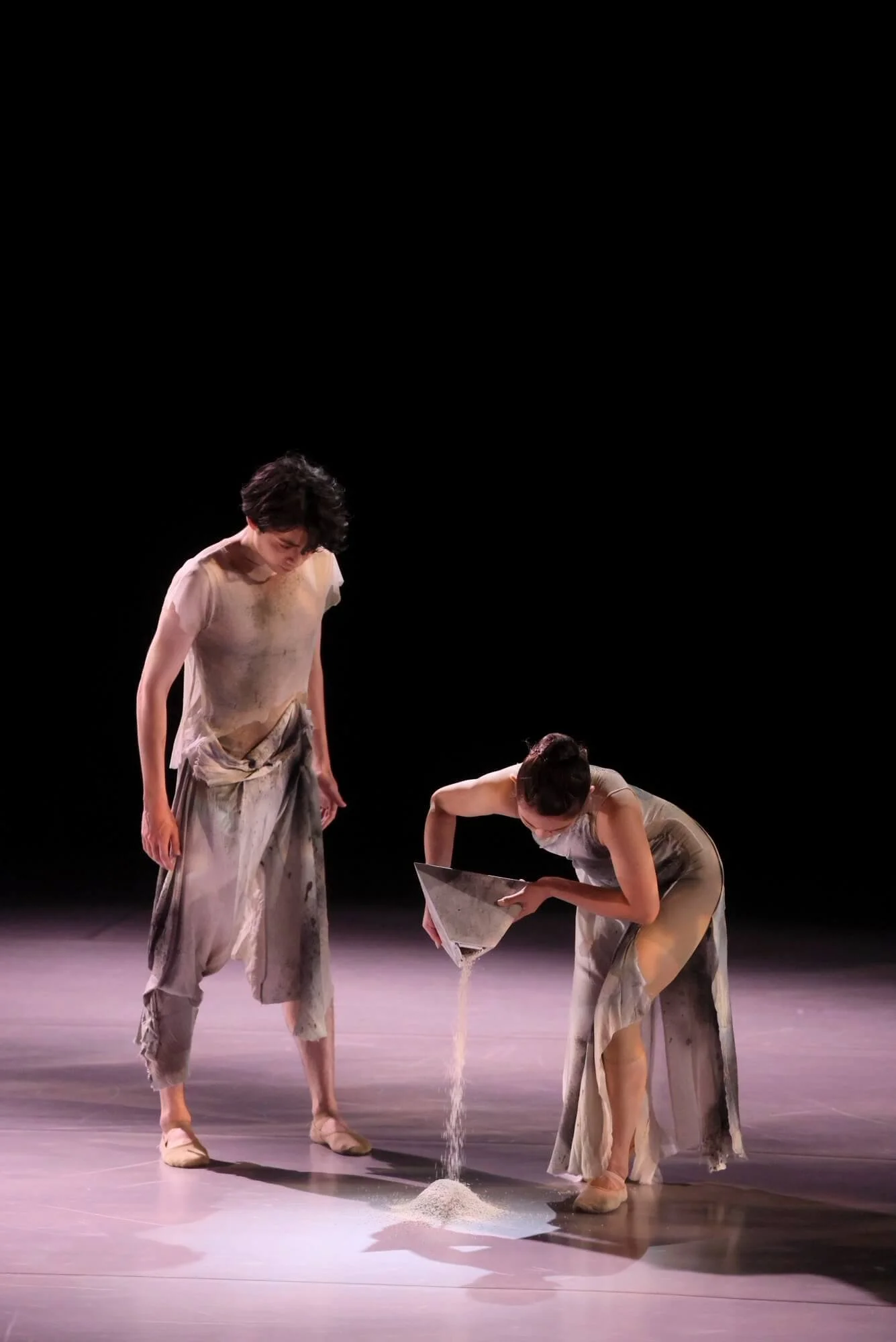 舞台上で二人の女性が砂を使った演技をしている。女性たちは汚れた衣装を着ている。