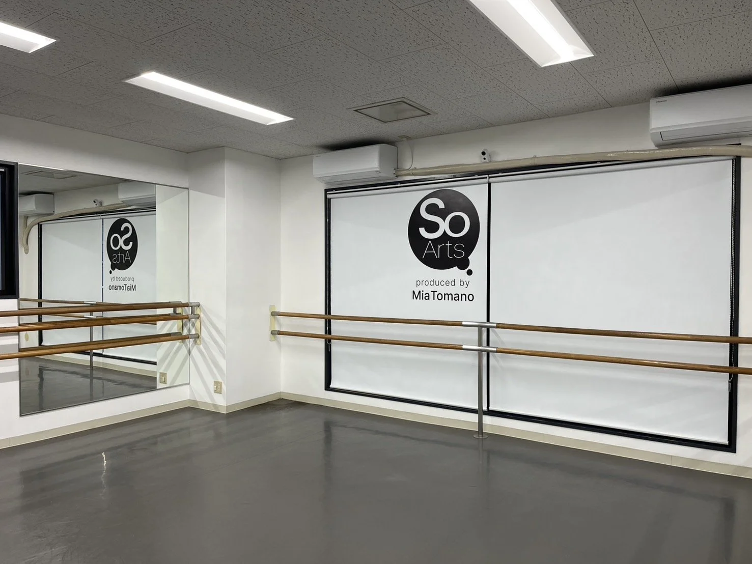 ダンススタジオの鏡とバー, 壁に『So Arts produced by Mia Tomano』のロゴと文字, 白と木のバー, グレーの床と白い壁と天井