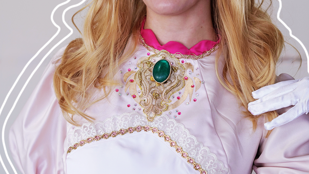 Close-up of the bodice of Princess Peach's costume, focusing on gold details and a bright teal stone, shot at PAX East 2026.