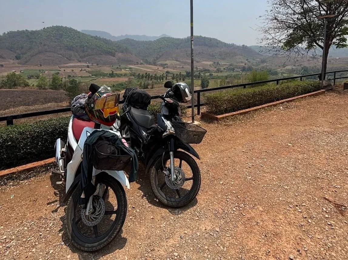 Two scooters parked in front of a hilly background along the Mae Hong Son Loop in Northern Thailand