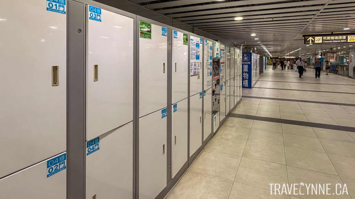 A row of white lockers in a large corridor of Taipei Main Station, with passengers walking in the distance