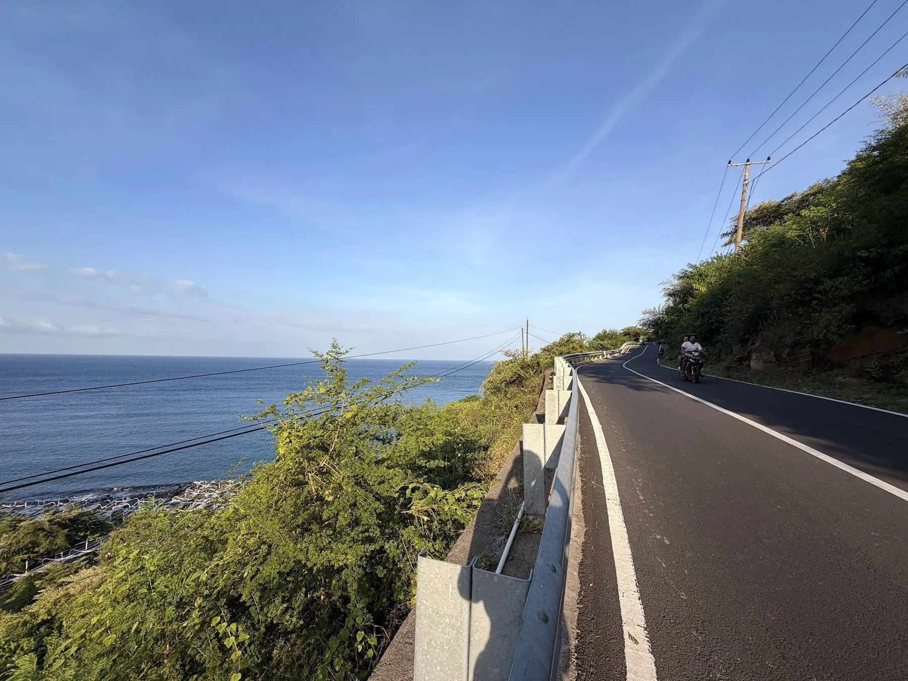 A paved road follows the coast with the sea in view in Amed, Bali