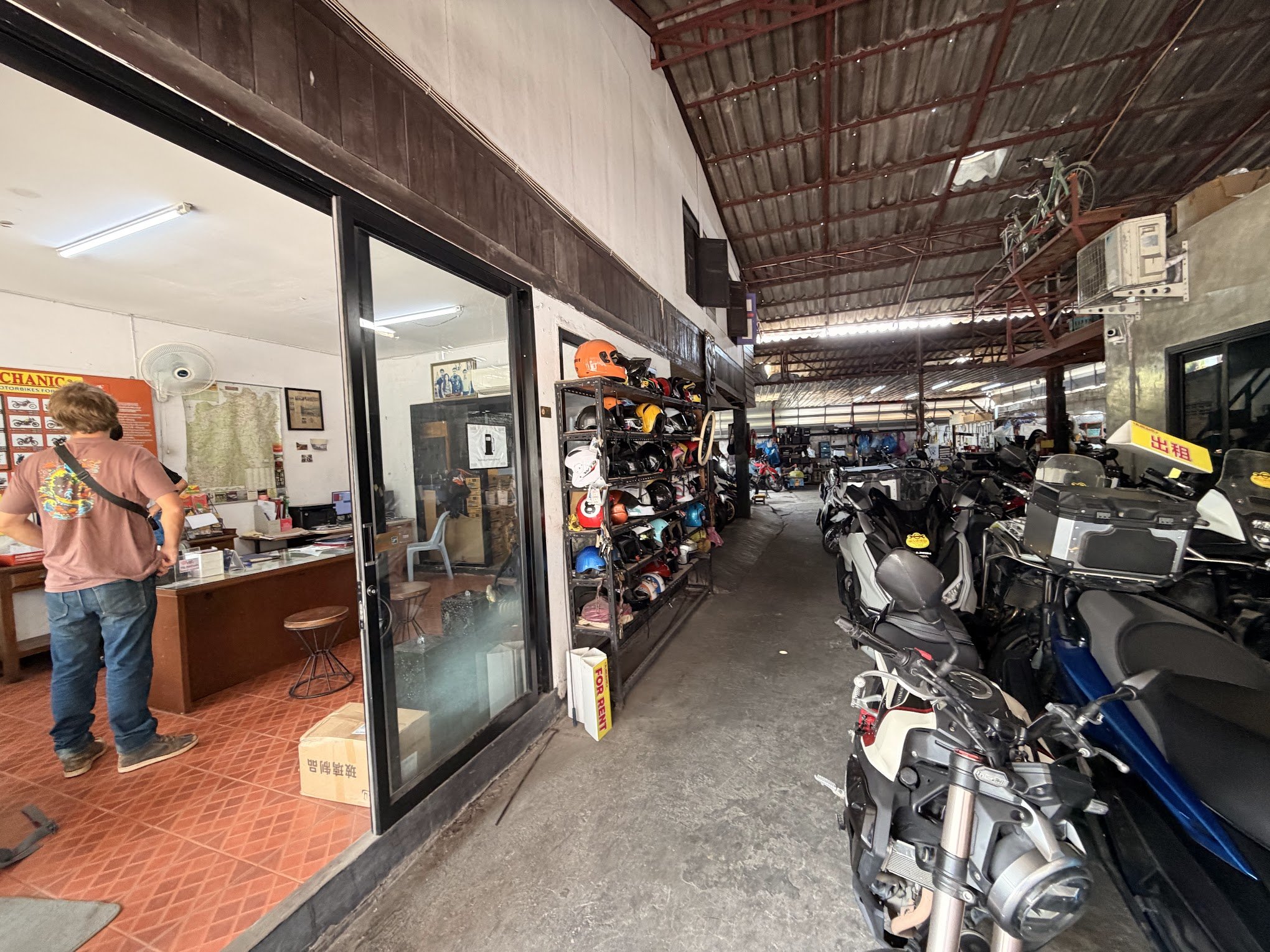 Inside Mr Mechanic 3 in Chiang Mai, Thailand, with scooters and motorbikes parked on the right and a client in the office to the left