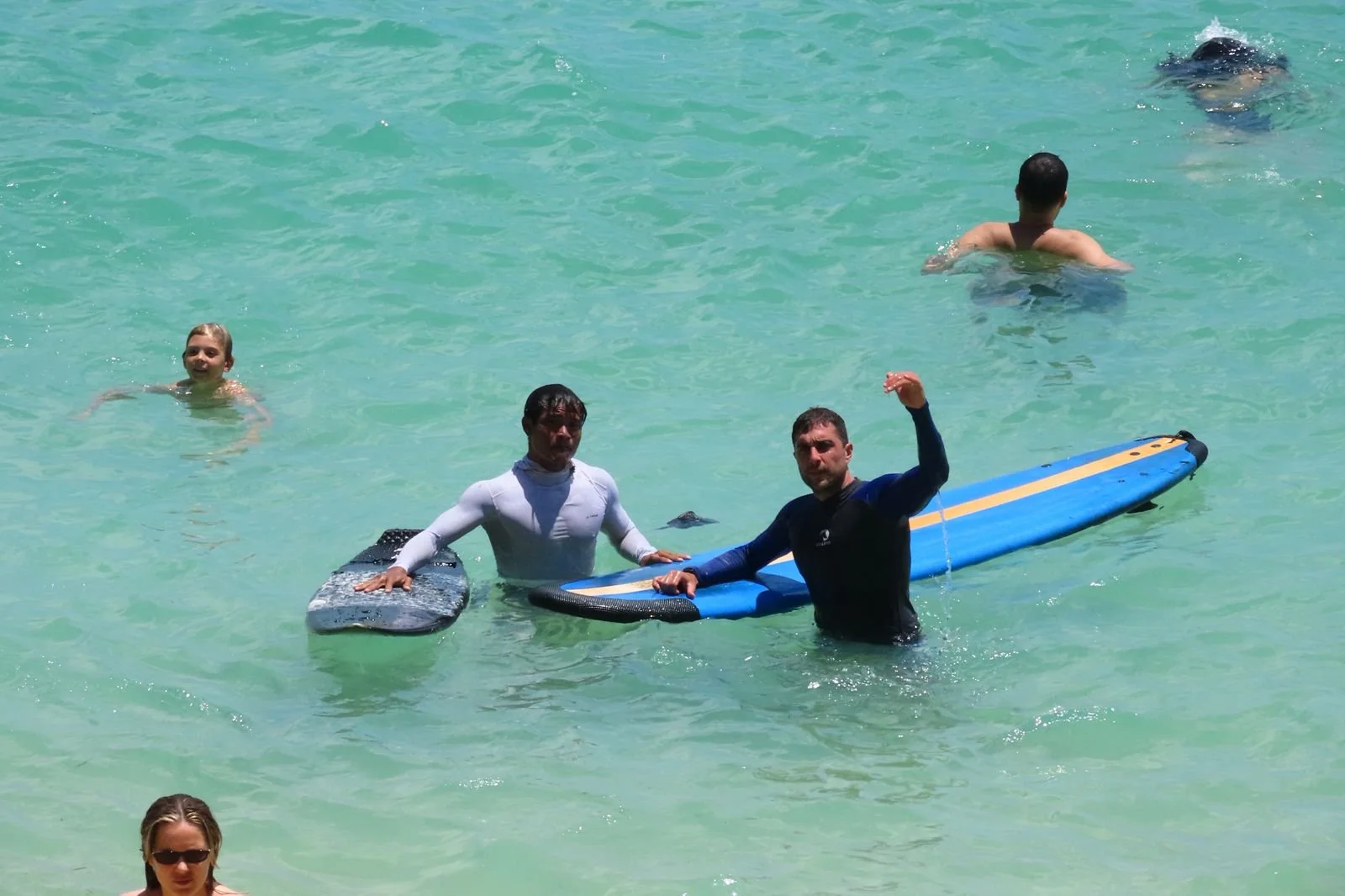 A surf instructor stands in shallow water with a student, each holding a board